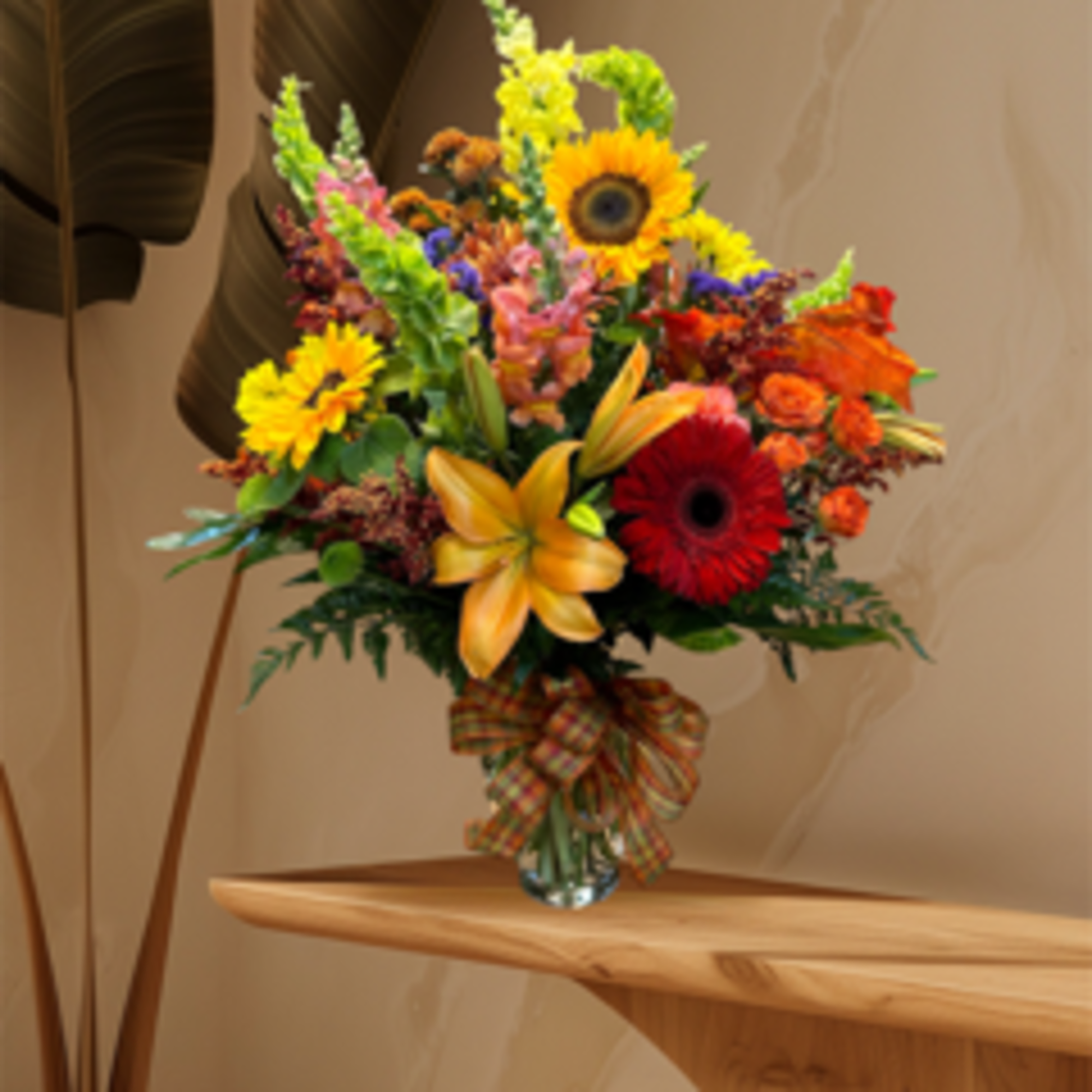 Colorful mixed flower bouquet in a clear glass vase with a plaid ribbon