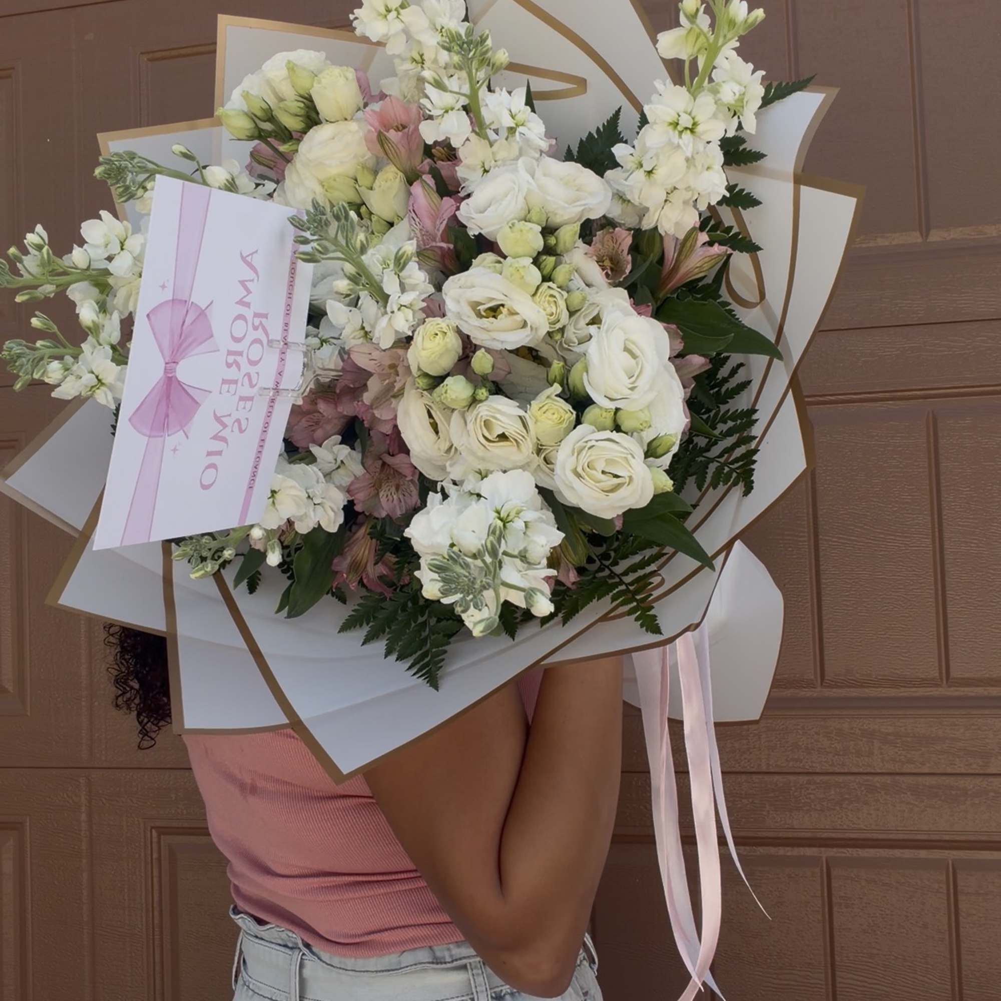 Large bouquet of white and blush flowers wrapped in white paper with pink ribbon