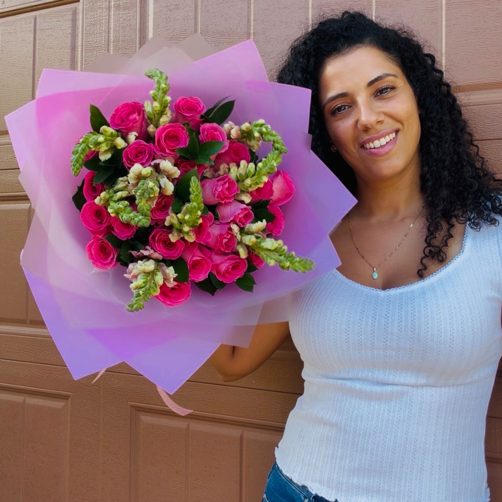 Woman holding a bouquet of bright pink roses wrapped in lavender paper
