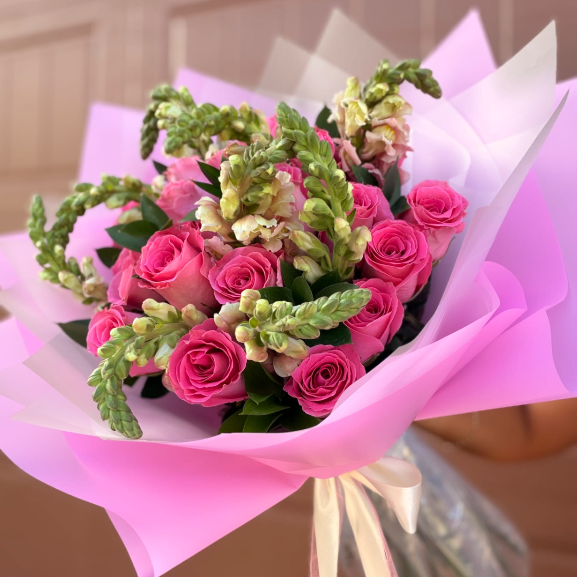 Bouquet of pink roses and pale snapdragons wrapped in pink paper