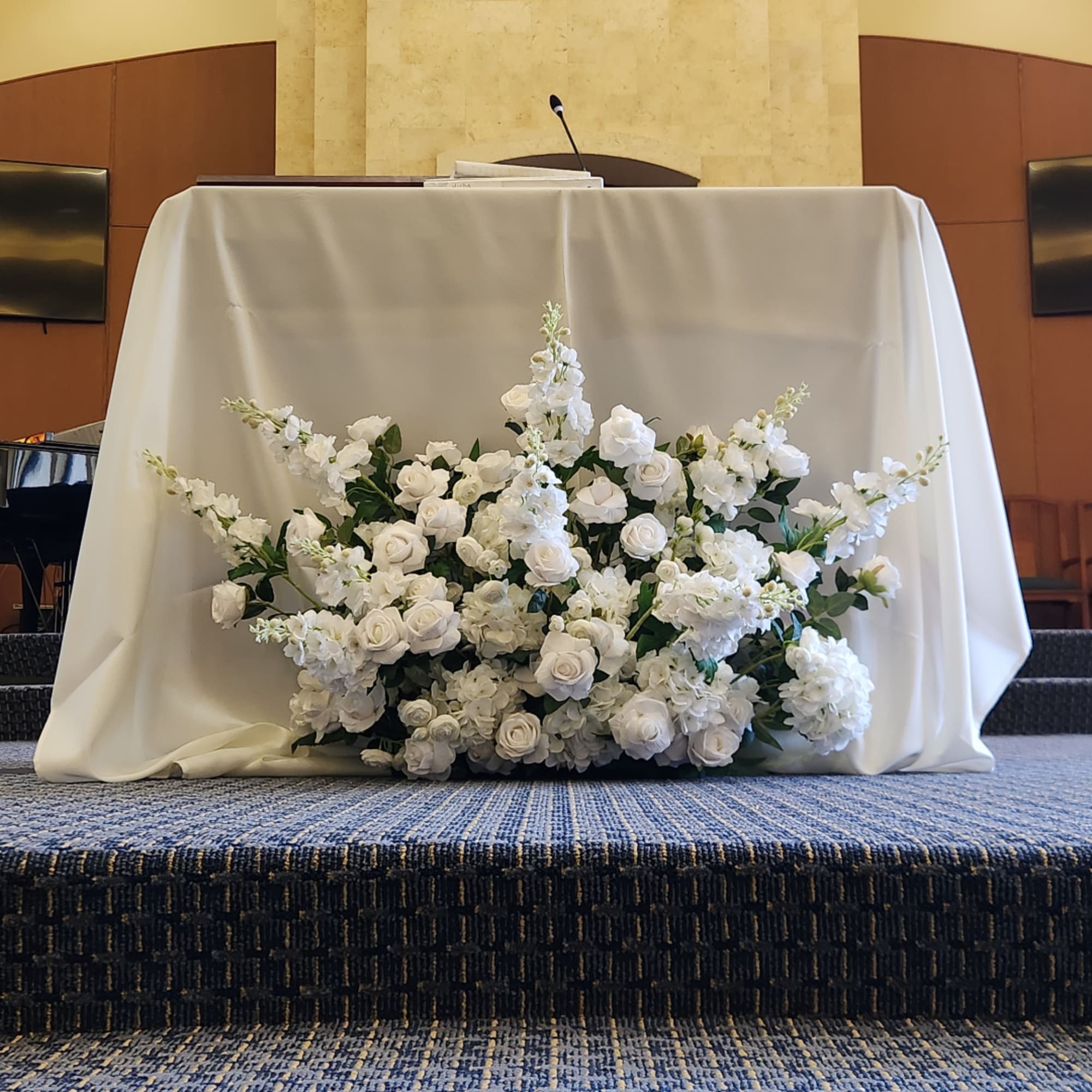 White floral arrangement on a draped table in a church or ceremony setting