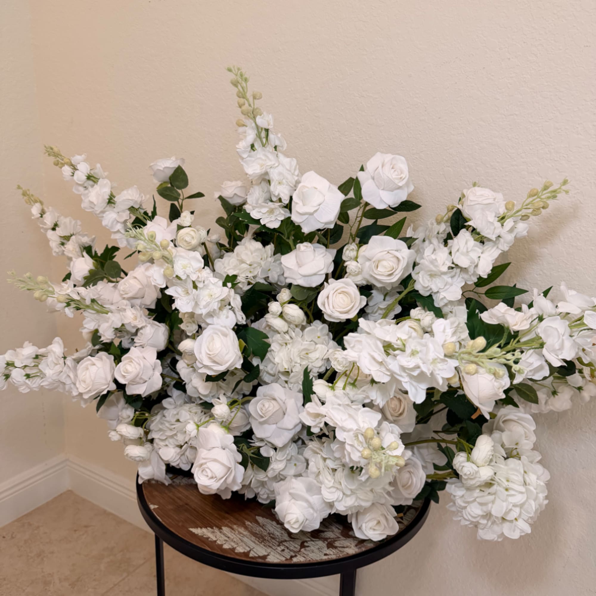 Large white floral arrangement with roses and snapdragons on a small table