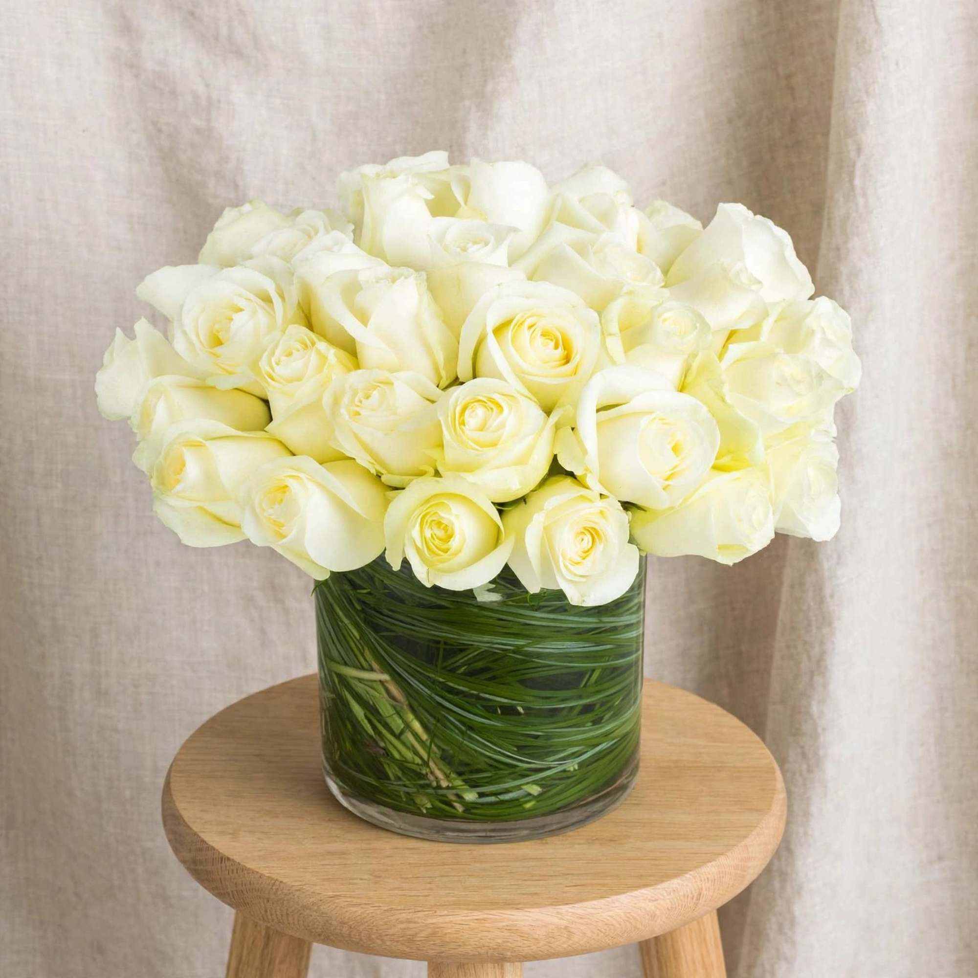 White rose bouquet in a clear glass vase on a wooden stool