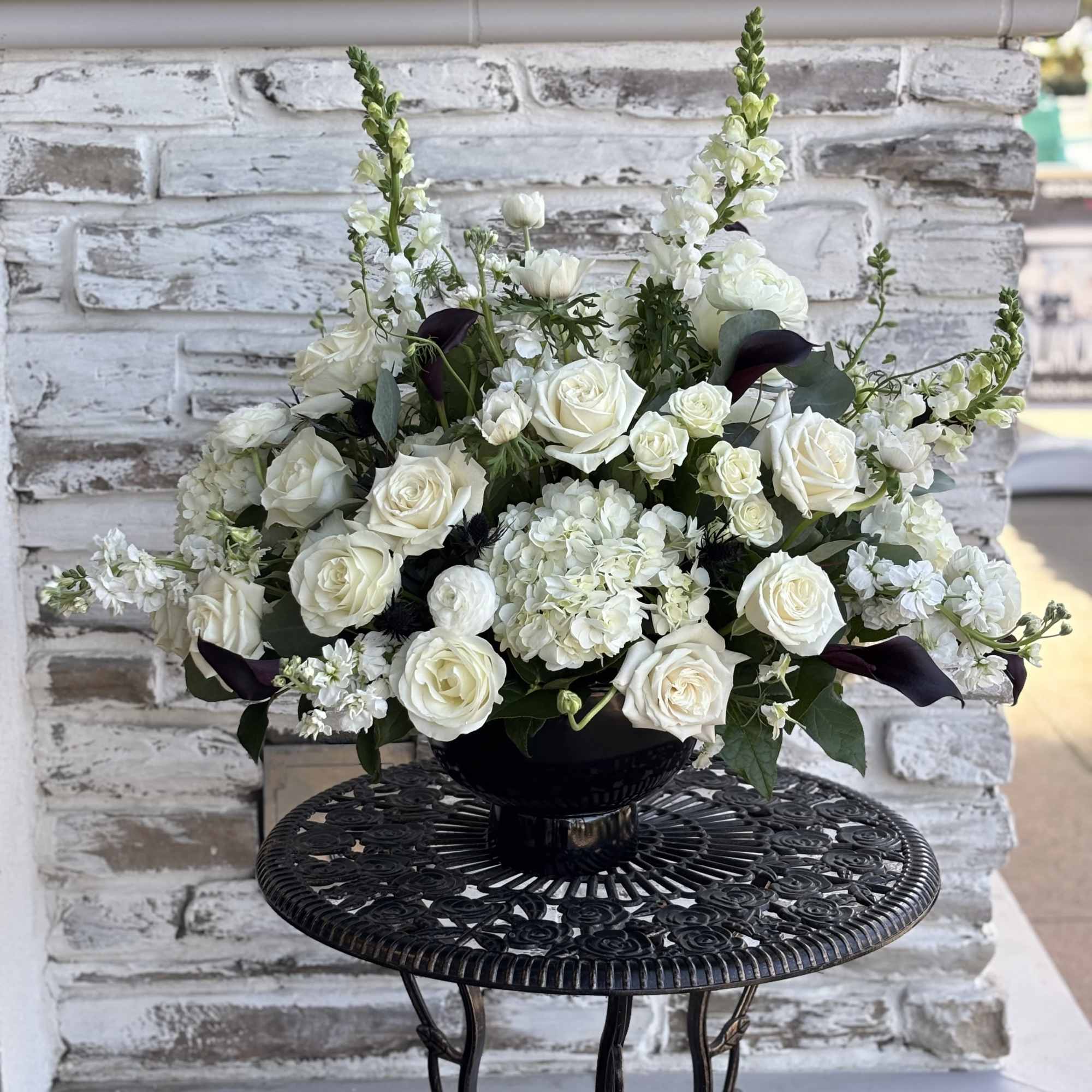 White rose arrangement in a black pedestal vase
