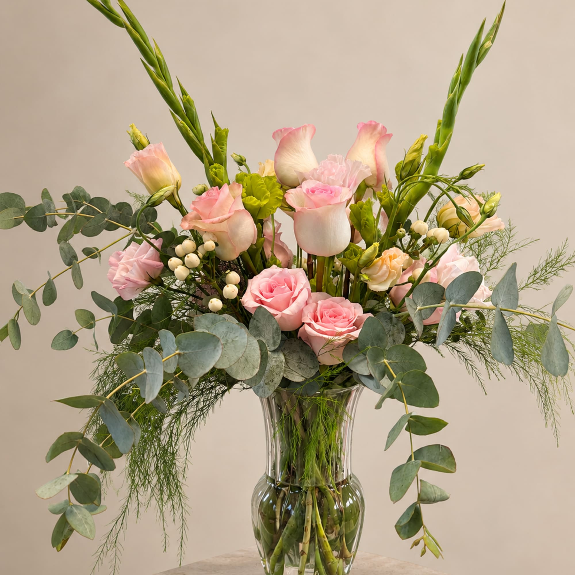 Pink roses and pale blooms arranged in a clear glass vase