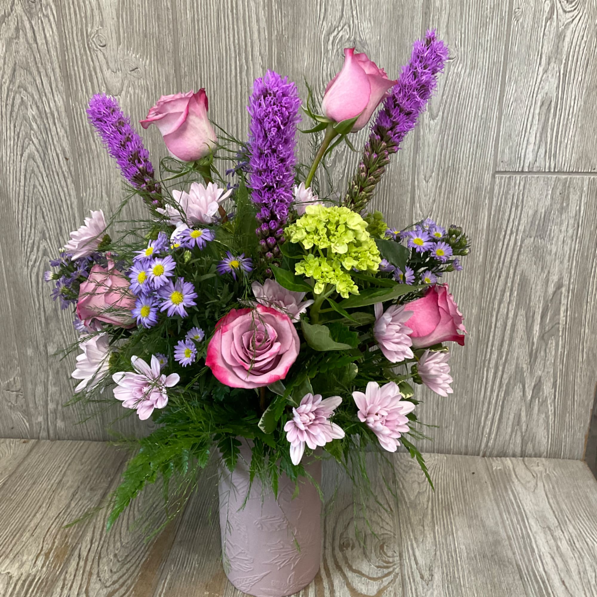 Pink roses and purple flowers arranged in a pink vase