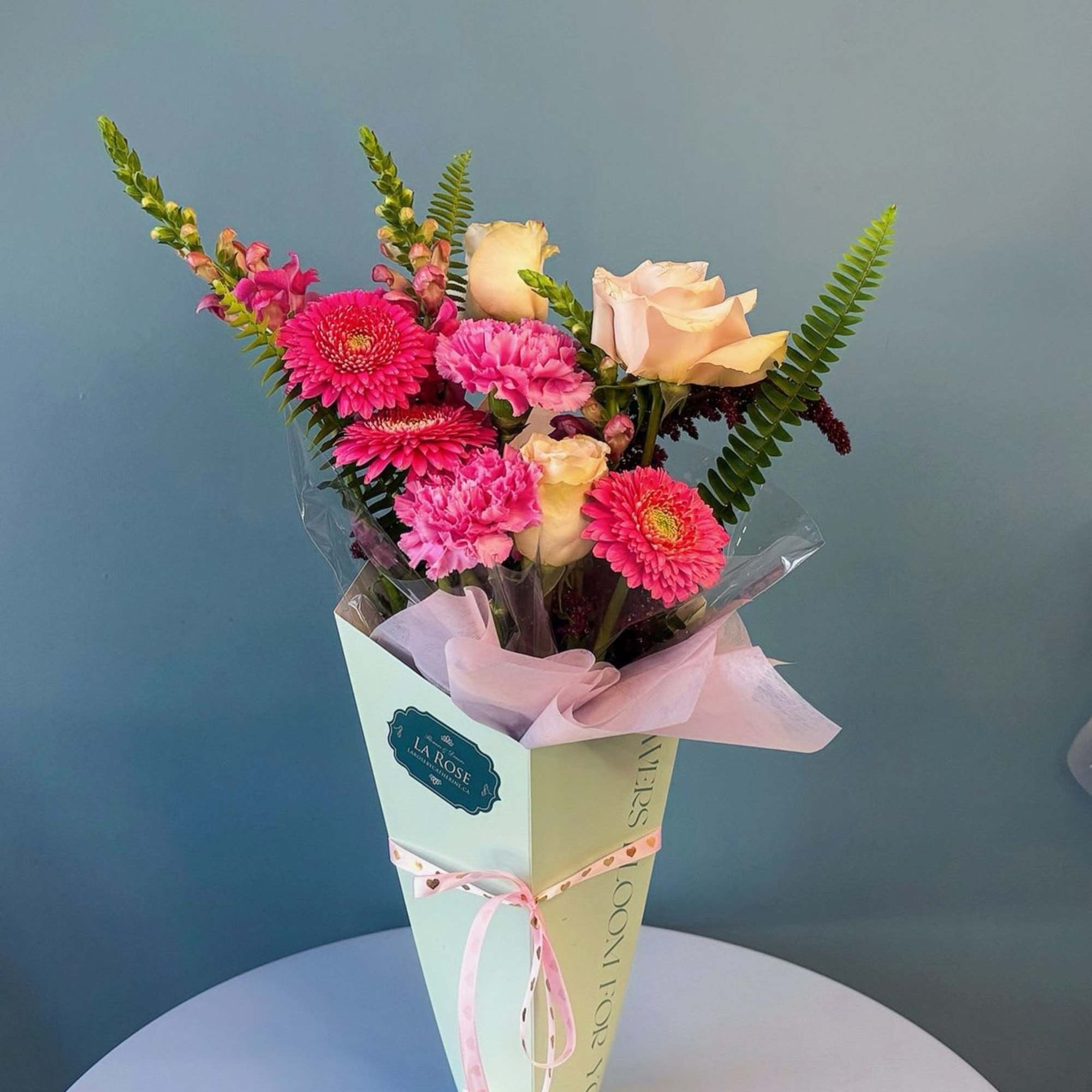 Bouquet of pink gerbera daisies, carnations, and pale roses in a pastel cone wrap
