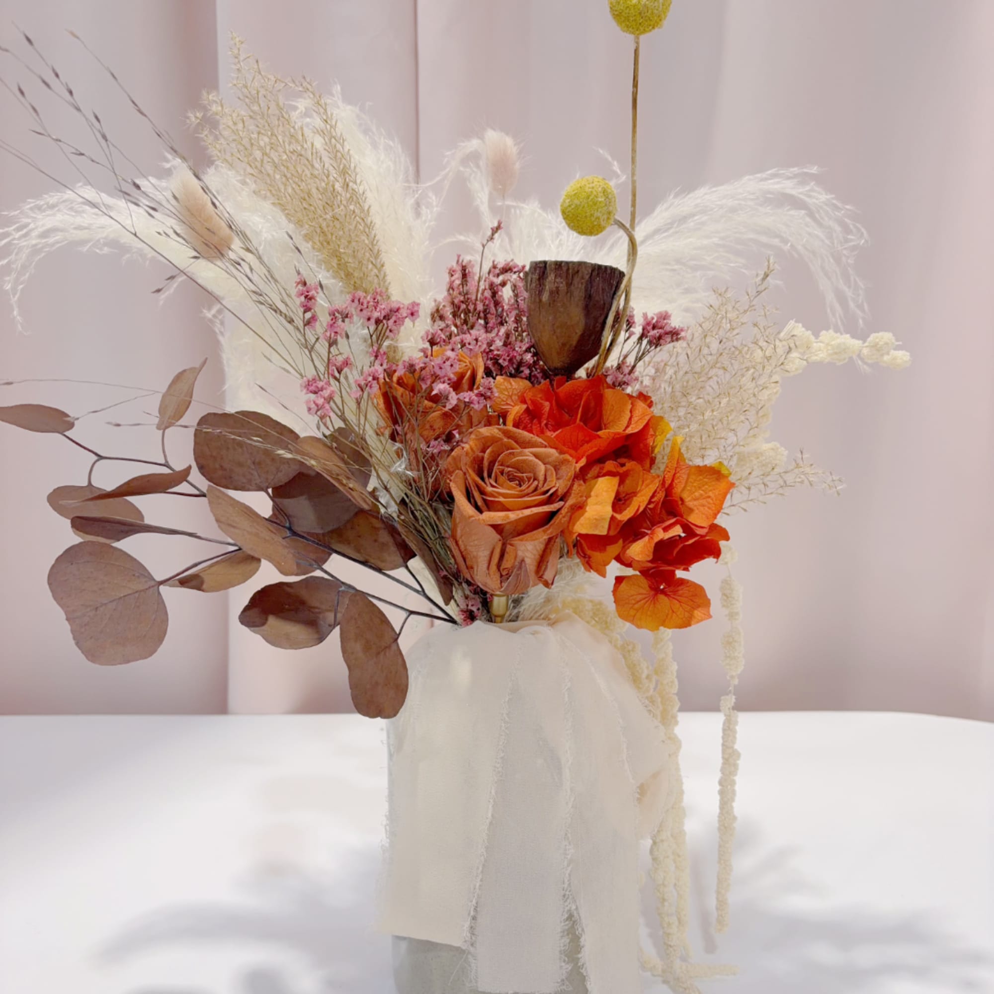 Dried floral arrangement with orange roses in a wrapped vase