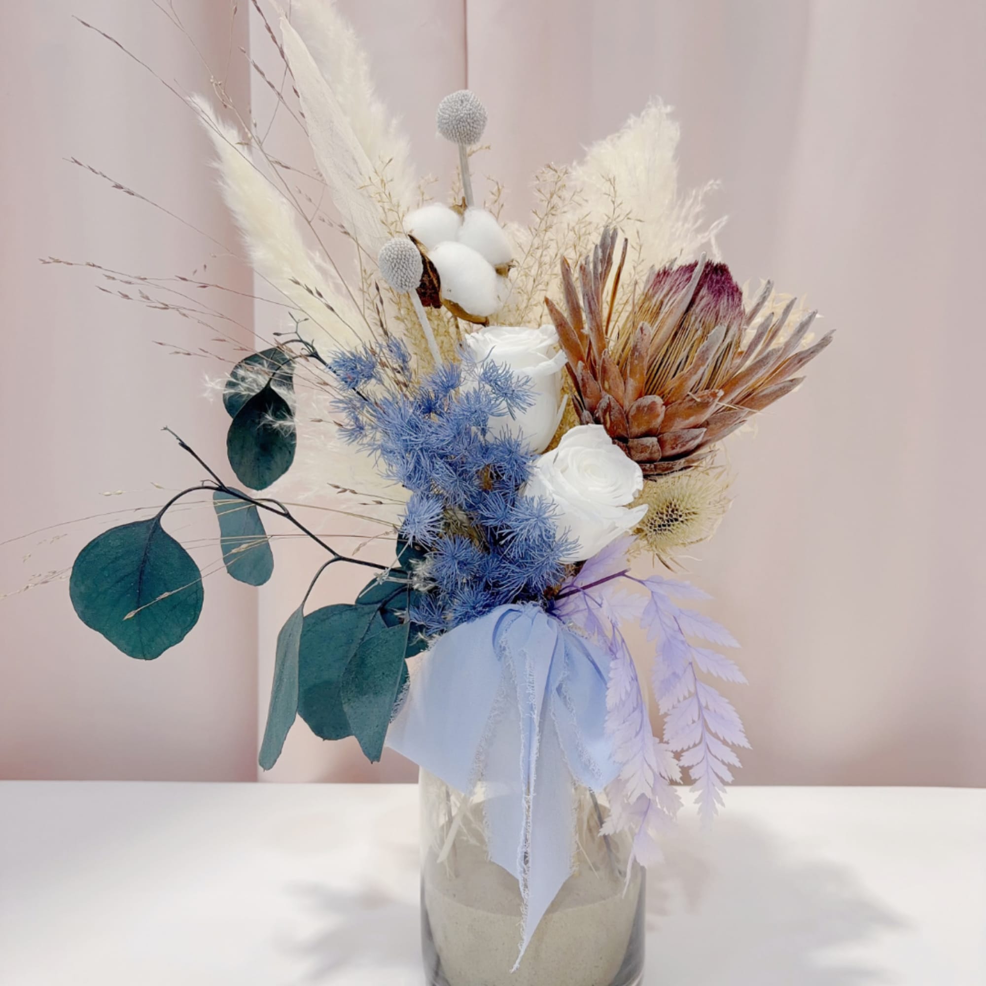 Dried floral arrangement in a glass vase with white and blue accents
