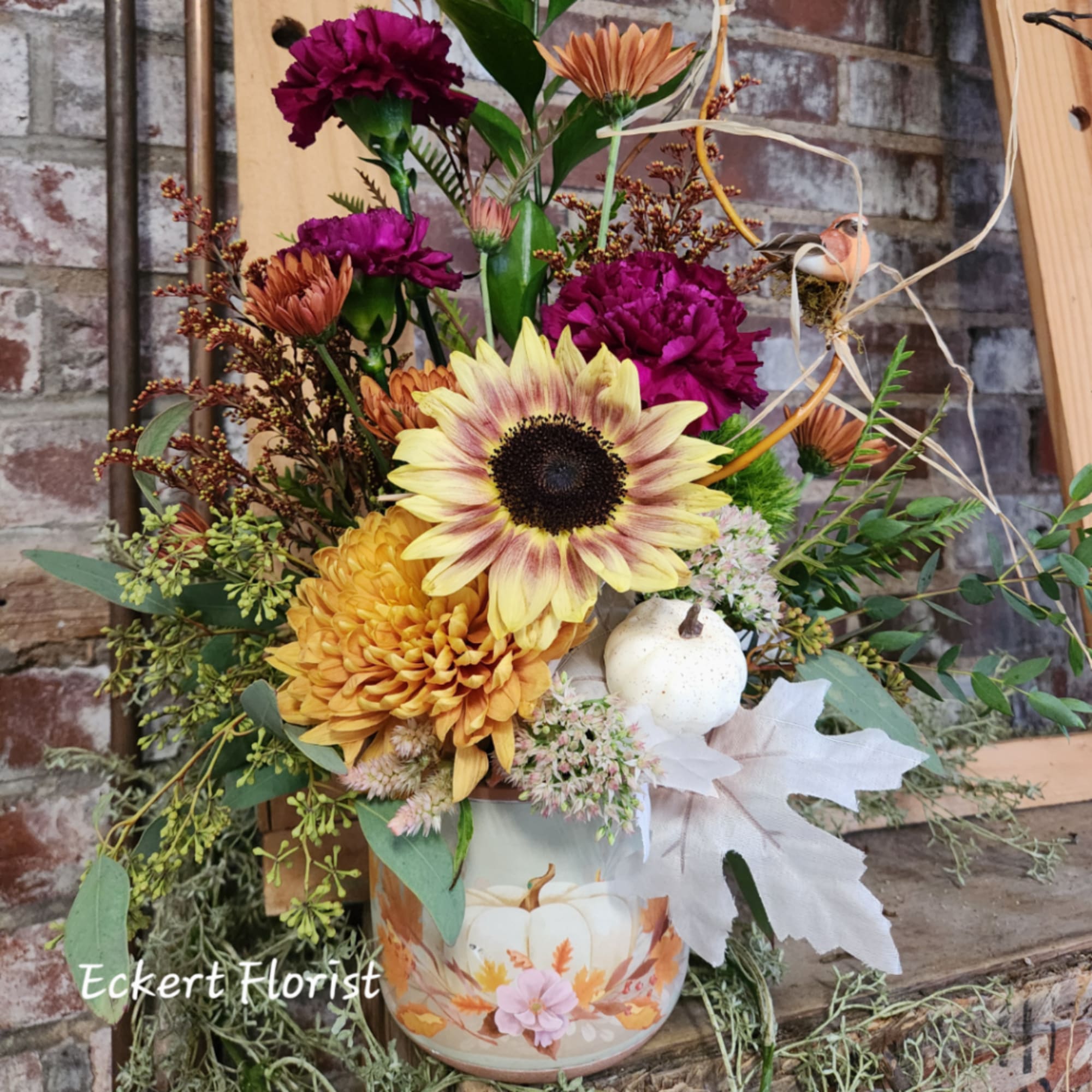 Fall floral arrangement in a pumpkin-decorated container with sunflowers and mums