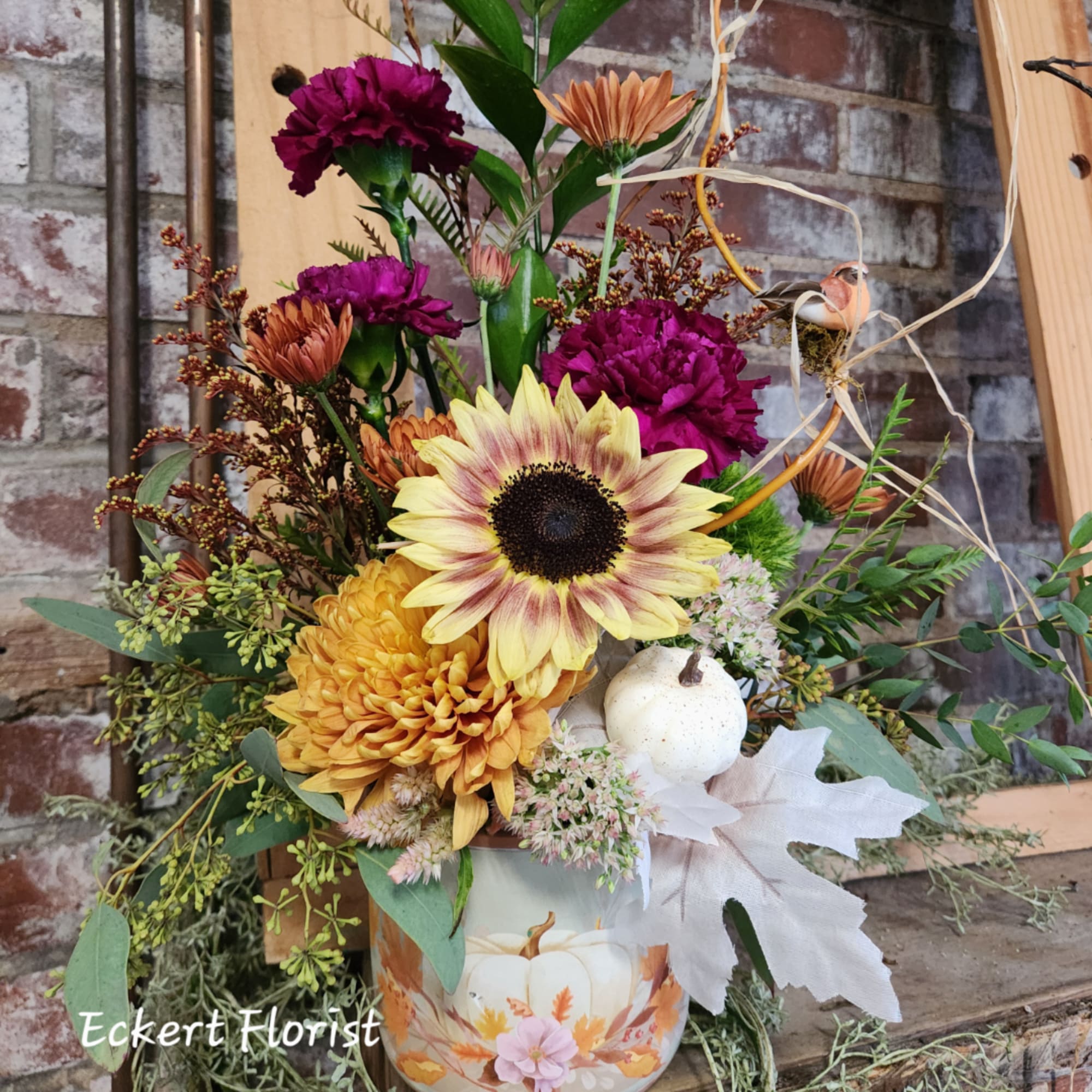 Mixed bouquet in a pumpkin-decorated container with a large sunflower and chrysanthemums