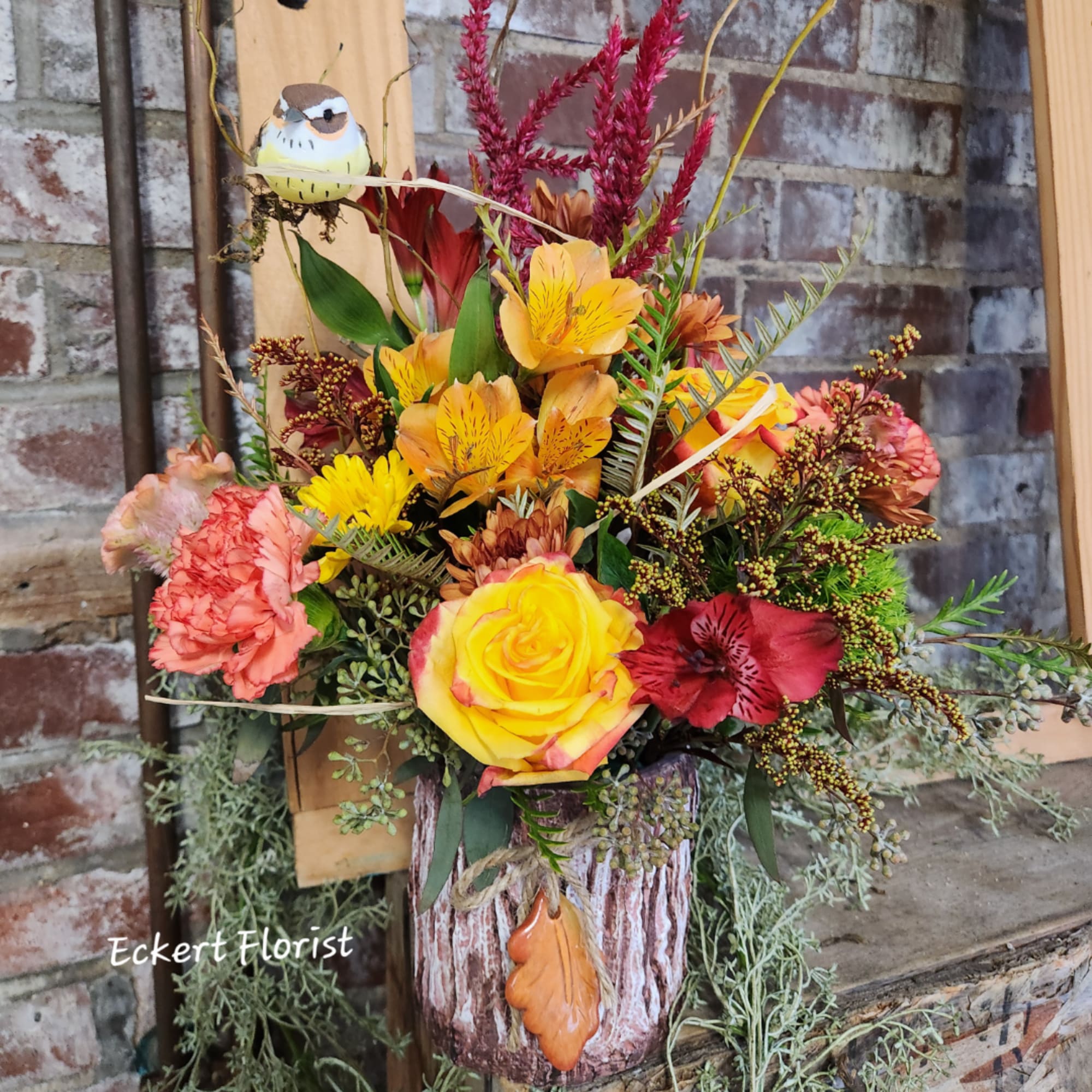 Colorful autumn bouquet in a rustic bark-covered container with a small bird ornament.