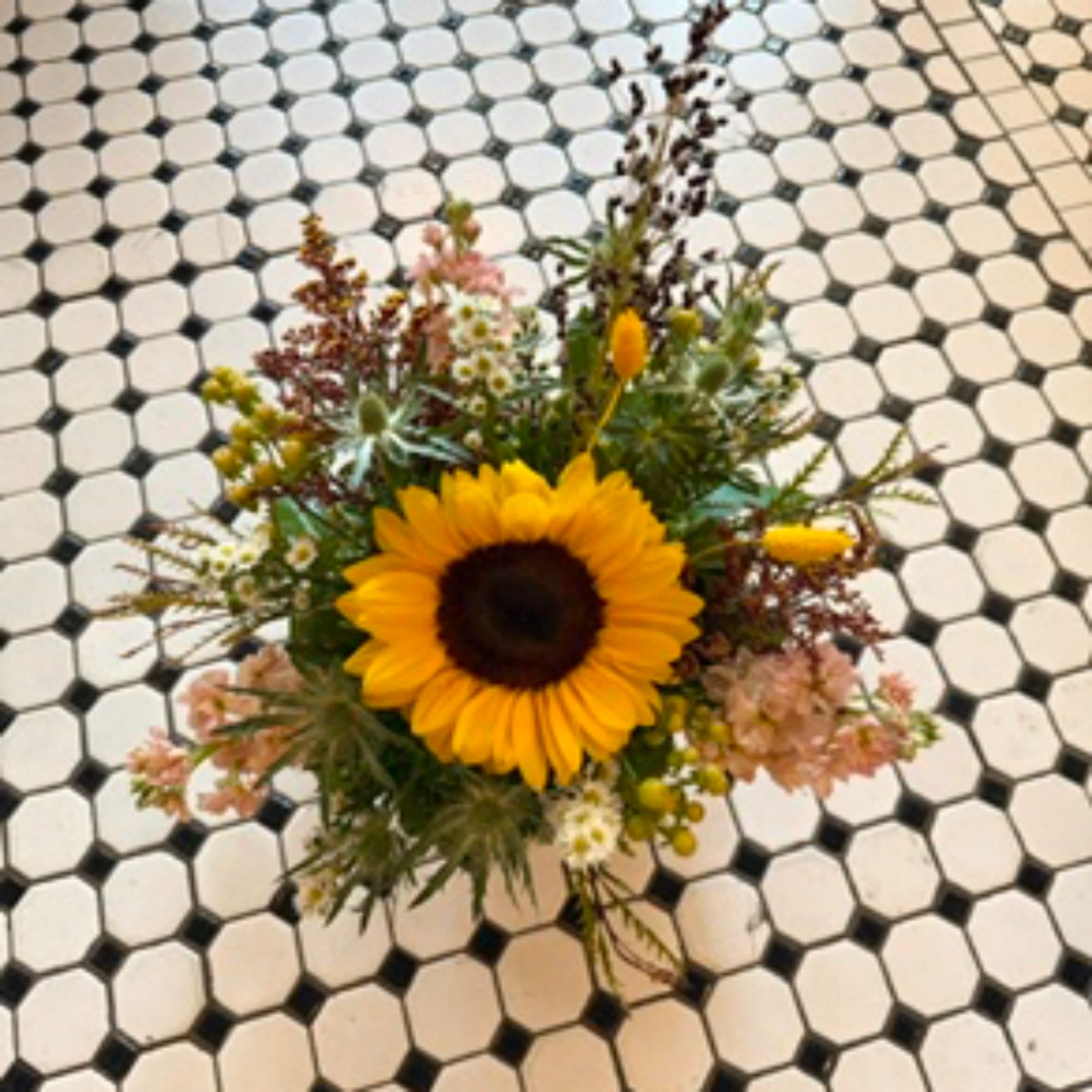 Sunflower bouquet with mixed small flowers on a tiled floor
