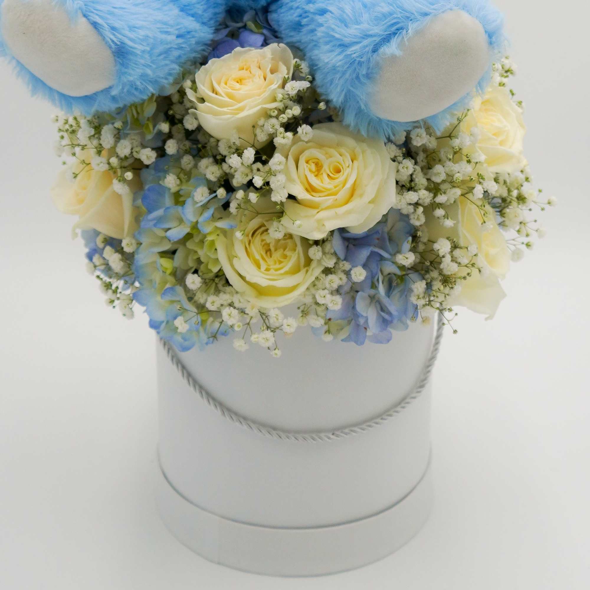 Blue teddy bear with a hatbox of cream and blue flowers