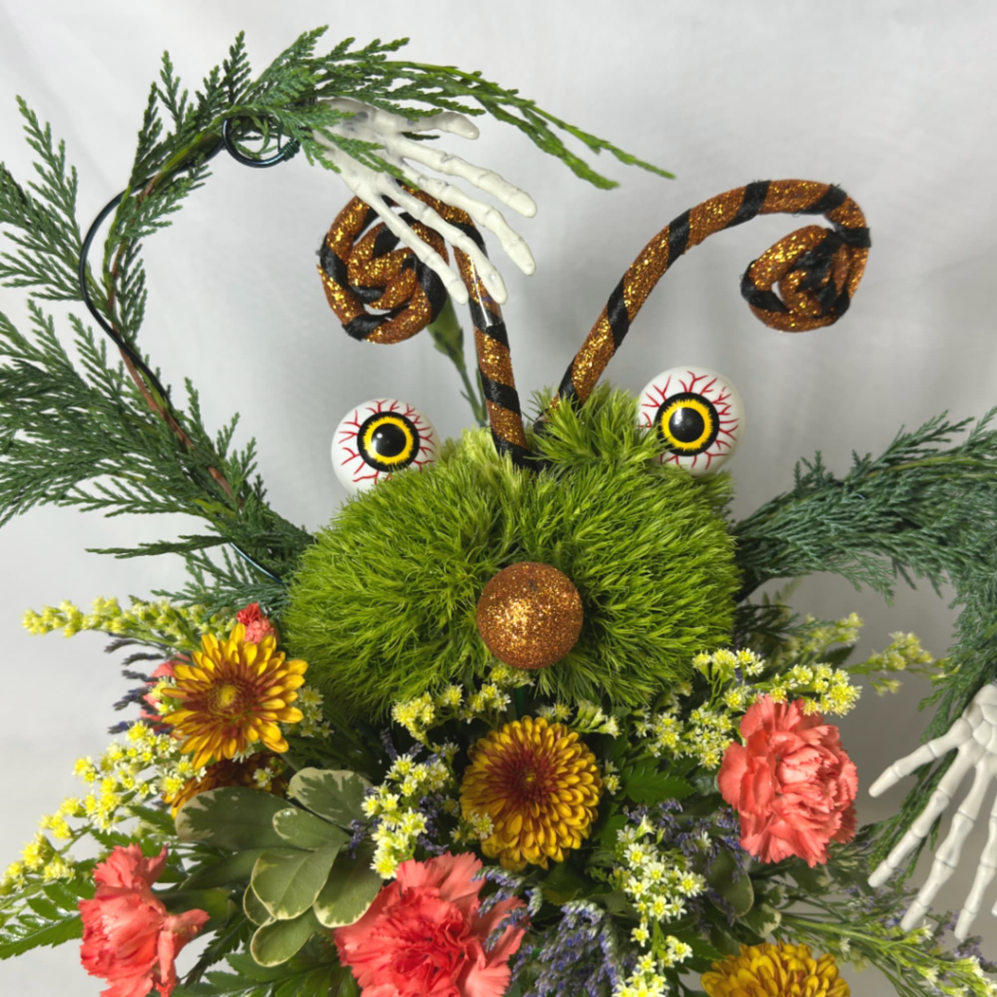 Halloween floral arrangement with a green fuzzy face, glittery antennae, and flowers