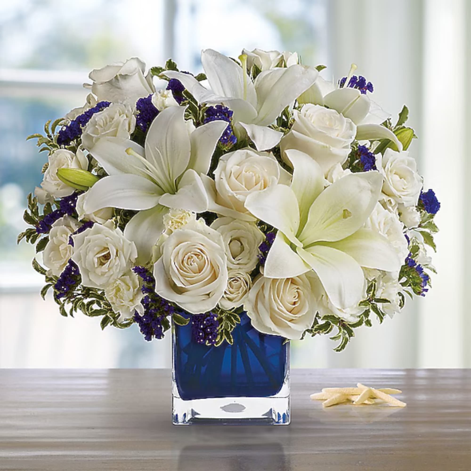 White roses and lilies arranged in a blue square vase