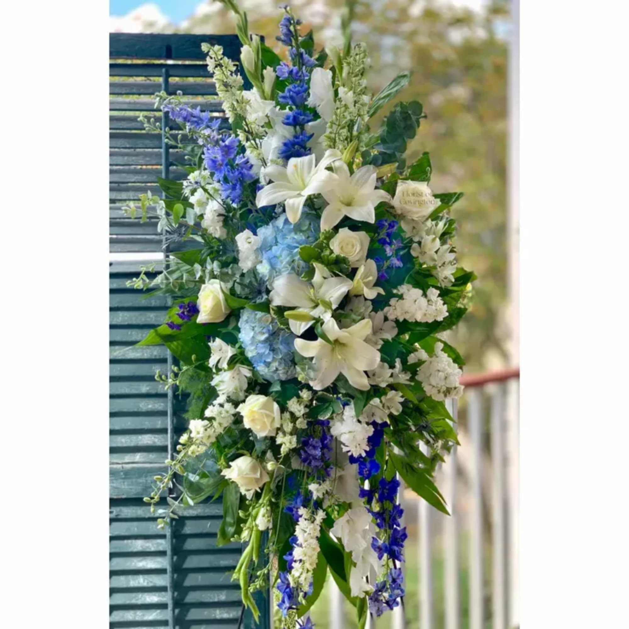 Tall floral spray with white lilies, blue flowers, and roses