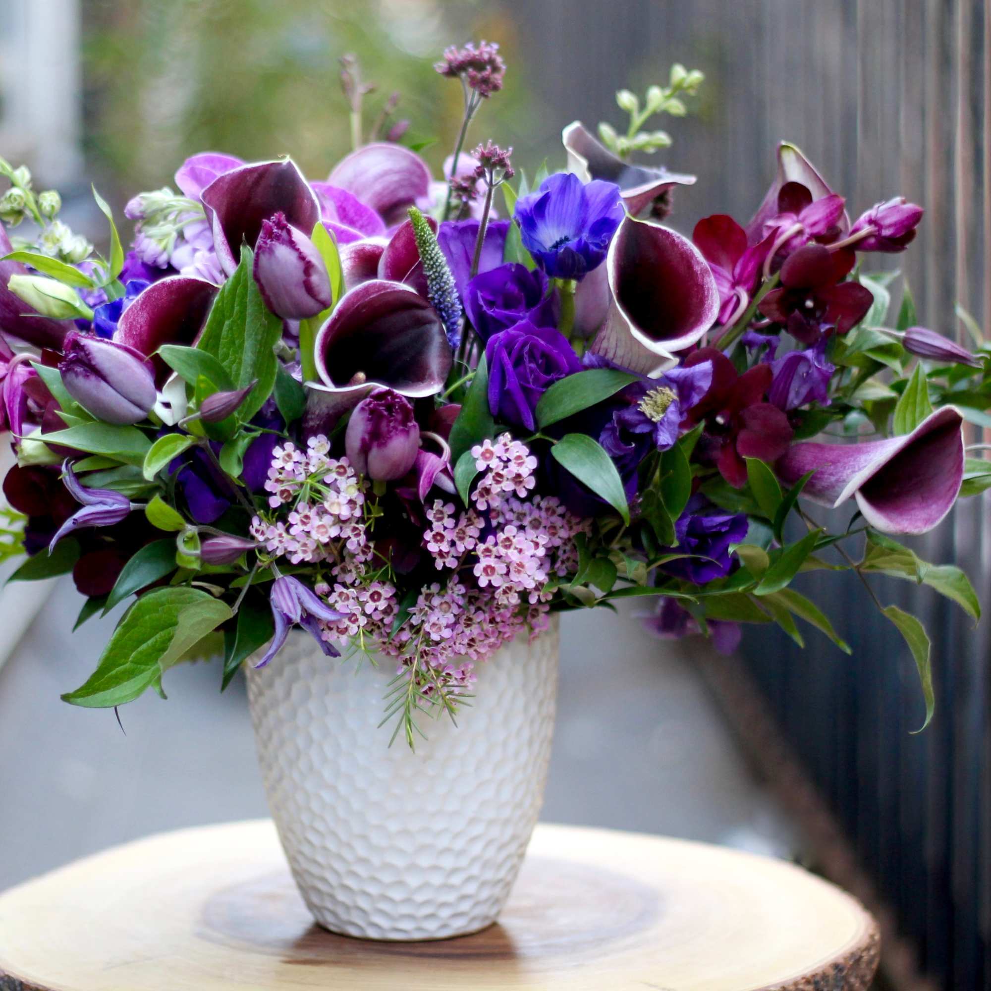 Purple and burgundy floral arrangement in a white textured vase