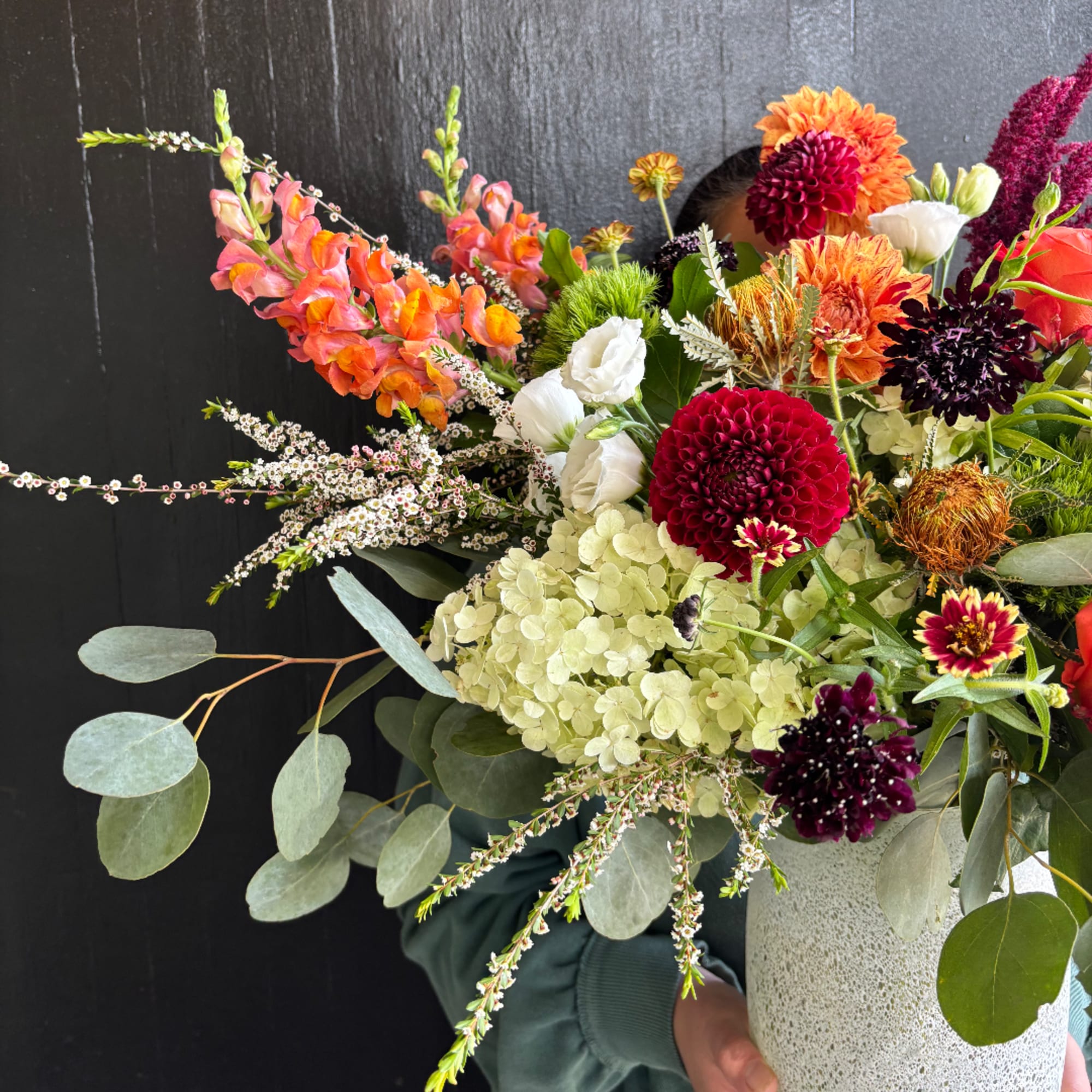 Colorful mixed bouquet in a speckled white vase with orange, white, and burgundy blooms.