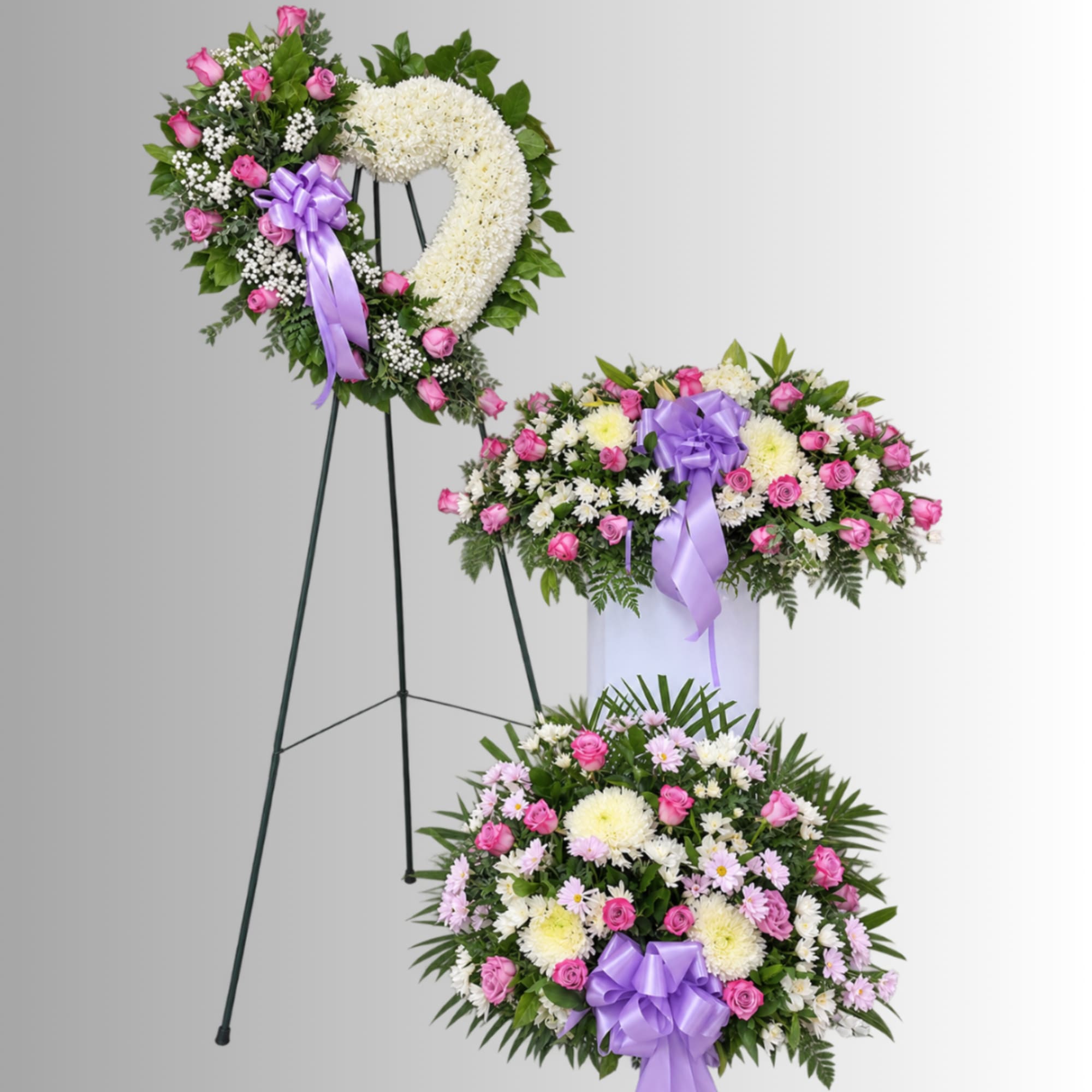 Three floral sympathy pieces with pink and white flowers and purple ribbons on stands.