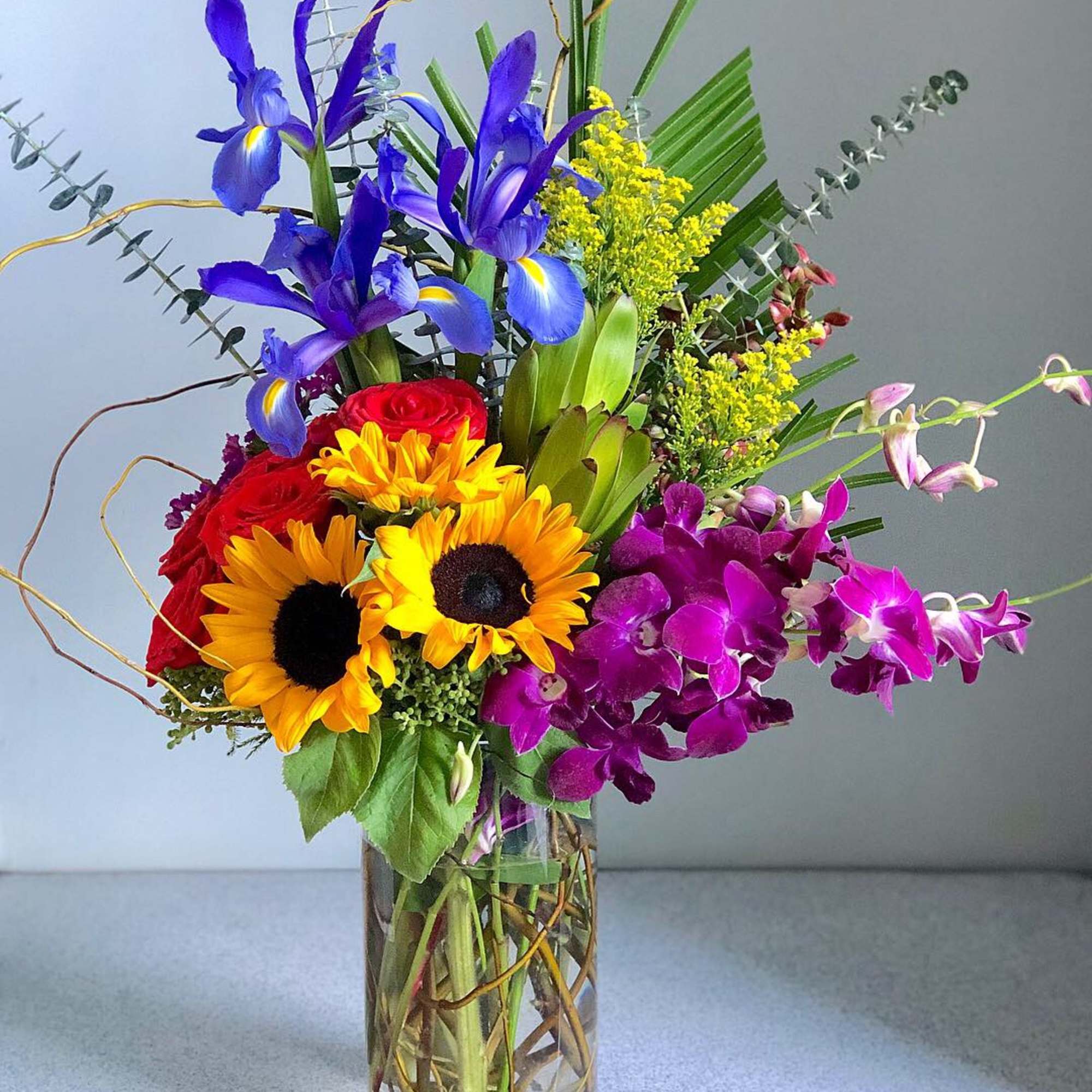Colorful bouquet with sunflowers, roses, irises, and orchids in a glass vase