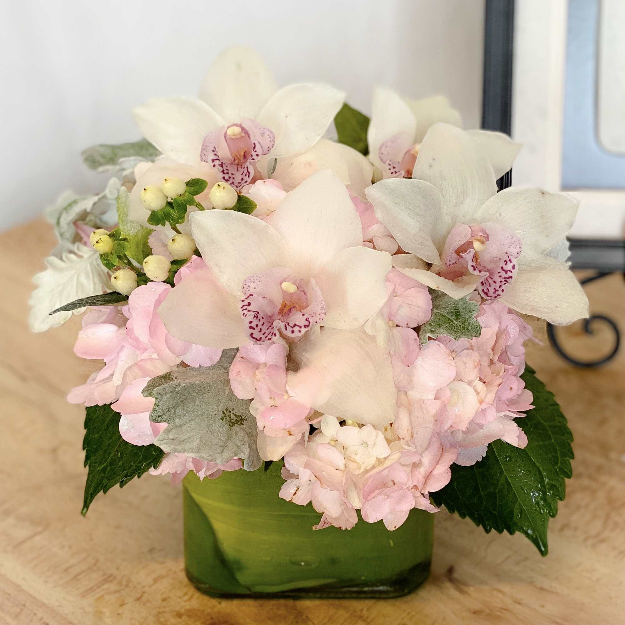 Pink and white orchid arrangement in a green glass vase