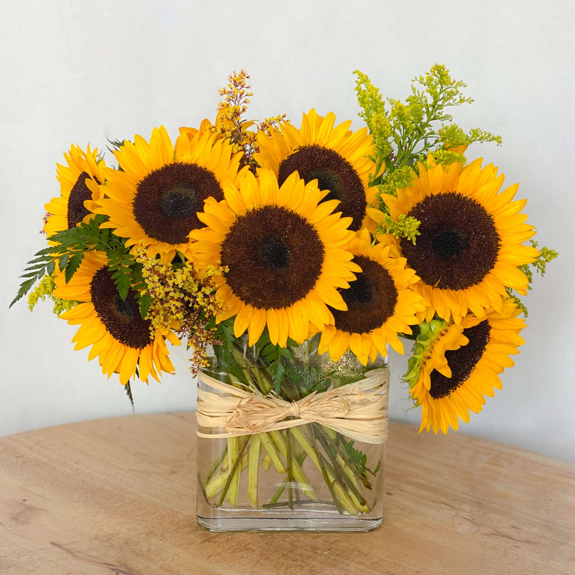 Sunflower bouquet in a clear square vase with a raffia bow