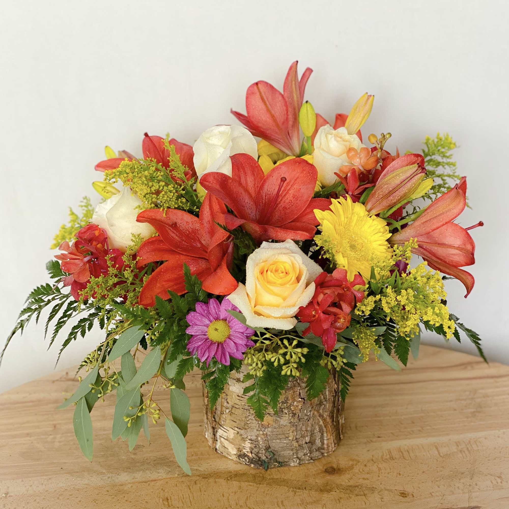 Colorful flower arrangement in a birch bark container with red lilies and roses