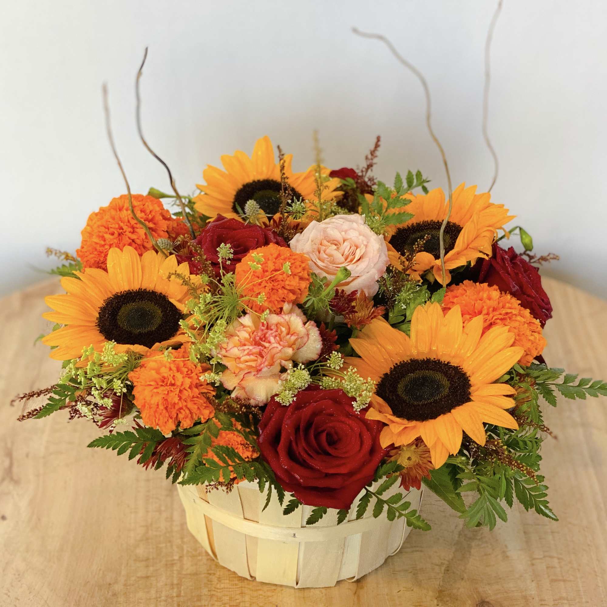 Basket arrangement with sunflowers, roses, and orange carnations