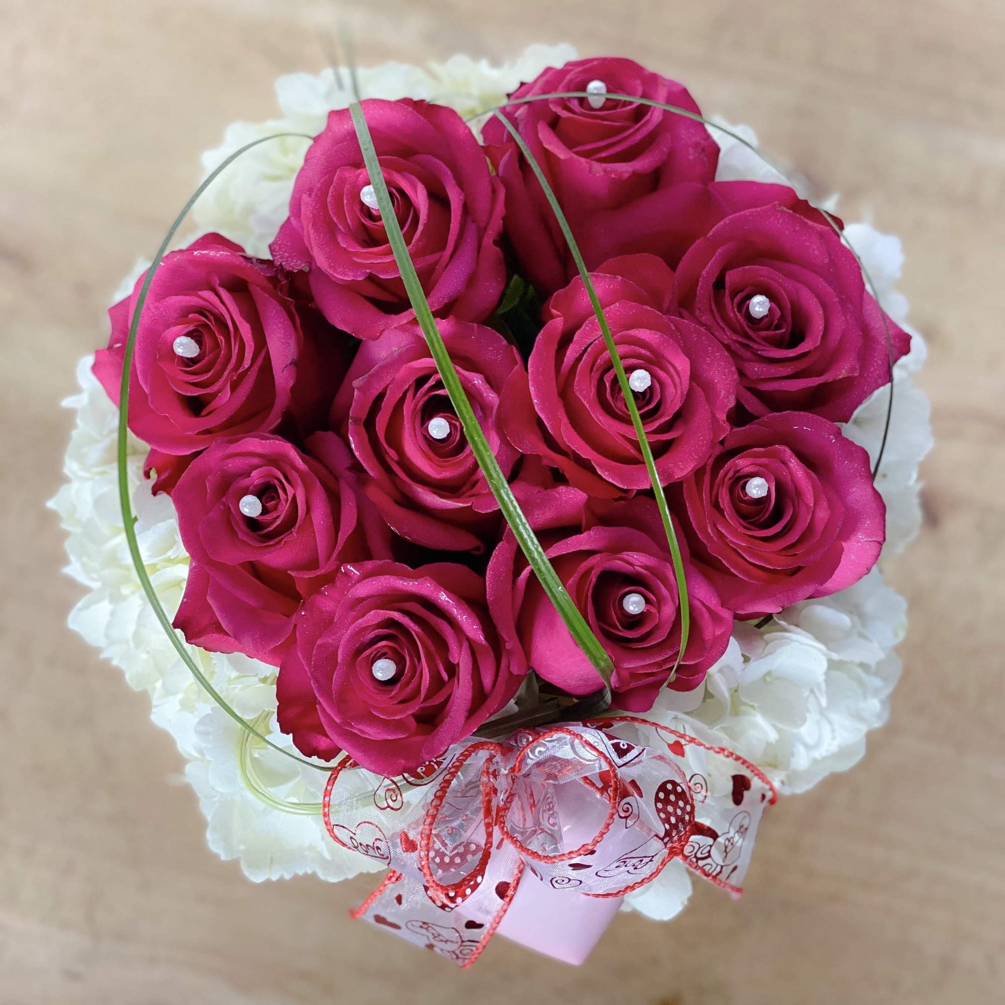Bouquet of hot pink roses with white flowers and a heart-patterned ribbon