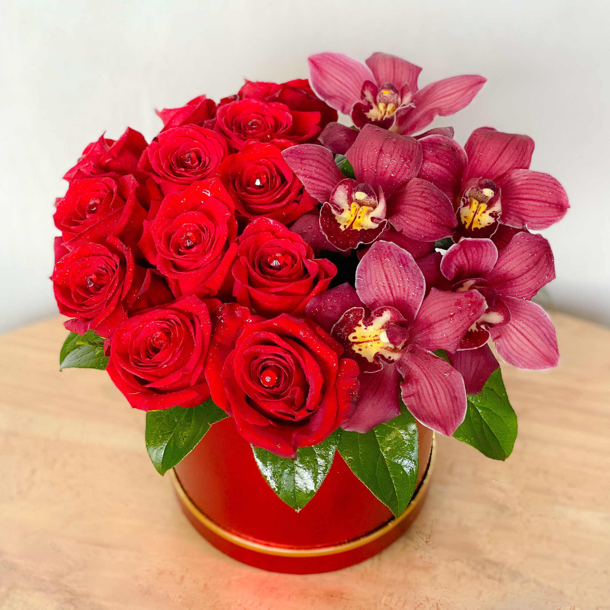 Red roses and pink orchids arranged in a round red box