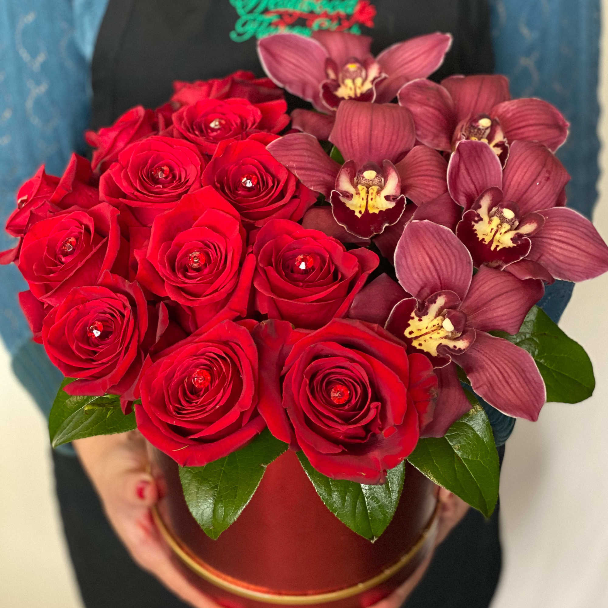 Red roses and burgundy orchids arranged in a round box
