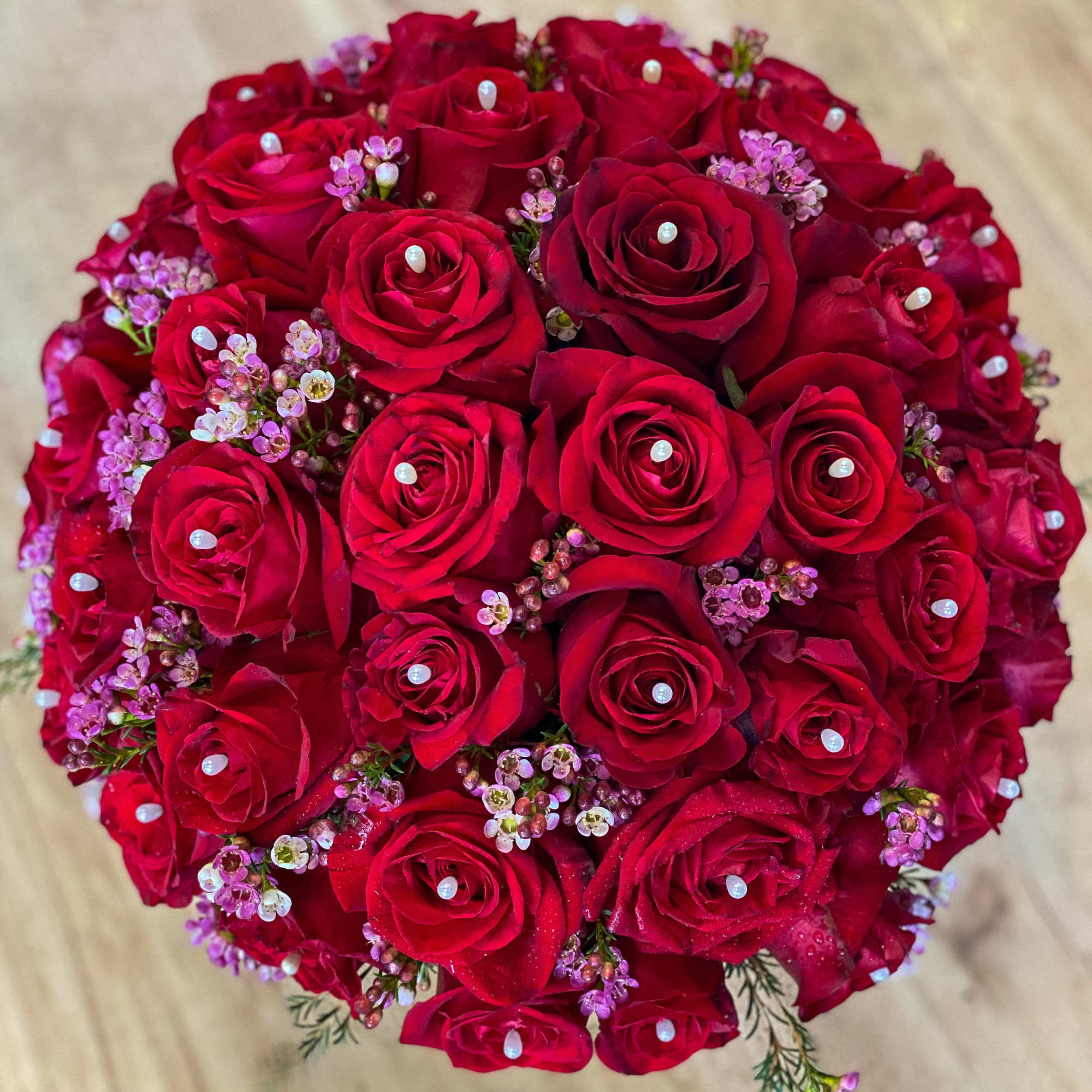 Round bouquet of red roses with small pink filler flowers and pearl accents