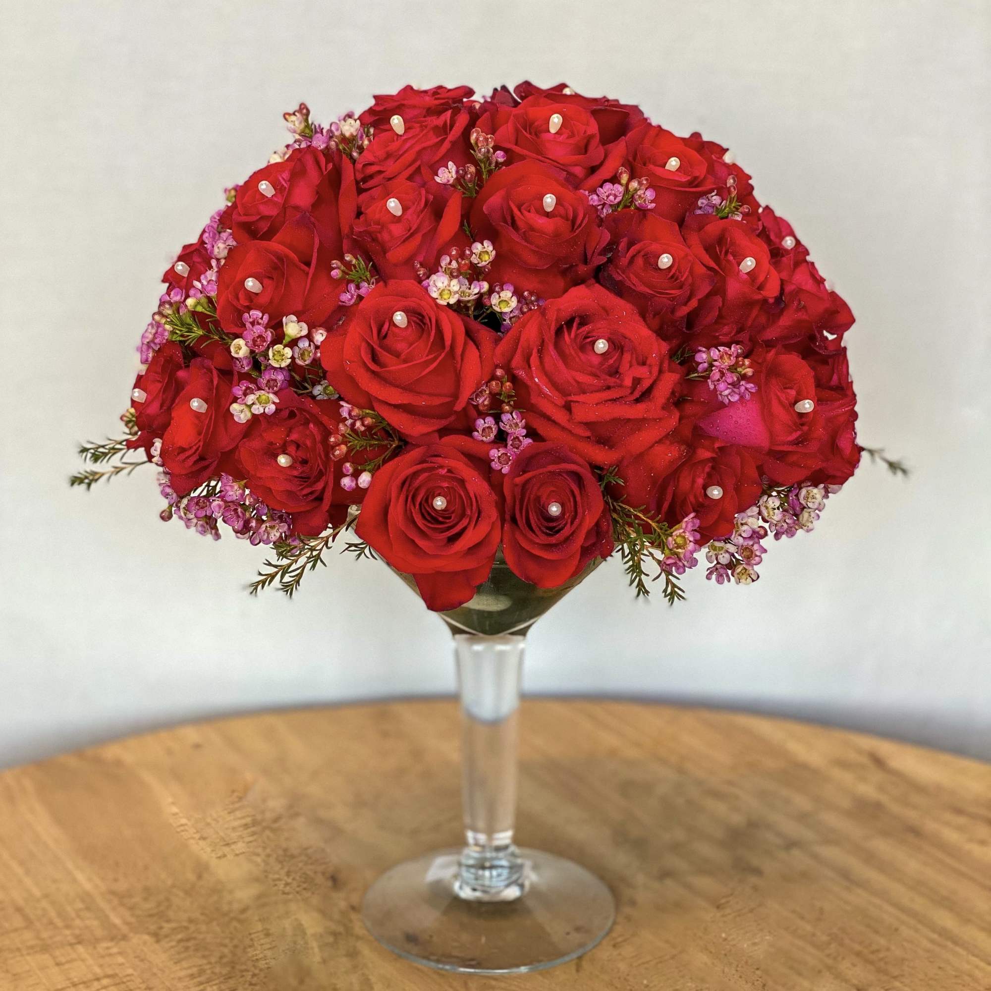 Red roses with small pink filler flowers in a stemmed glass vase