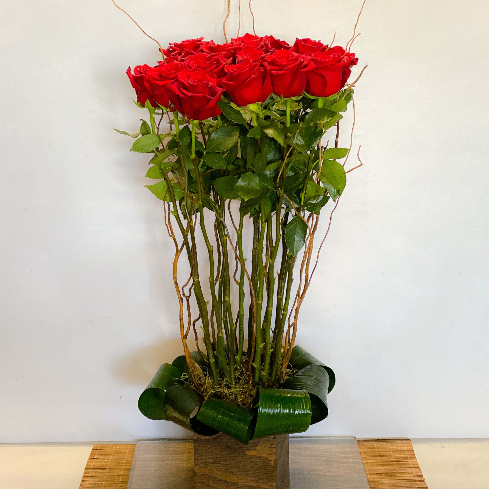 Tall arrangement of red roses with a decorative leaf base