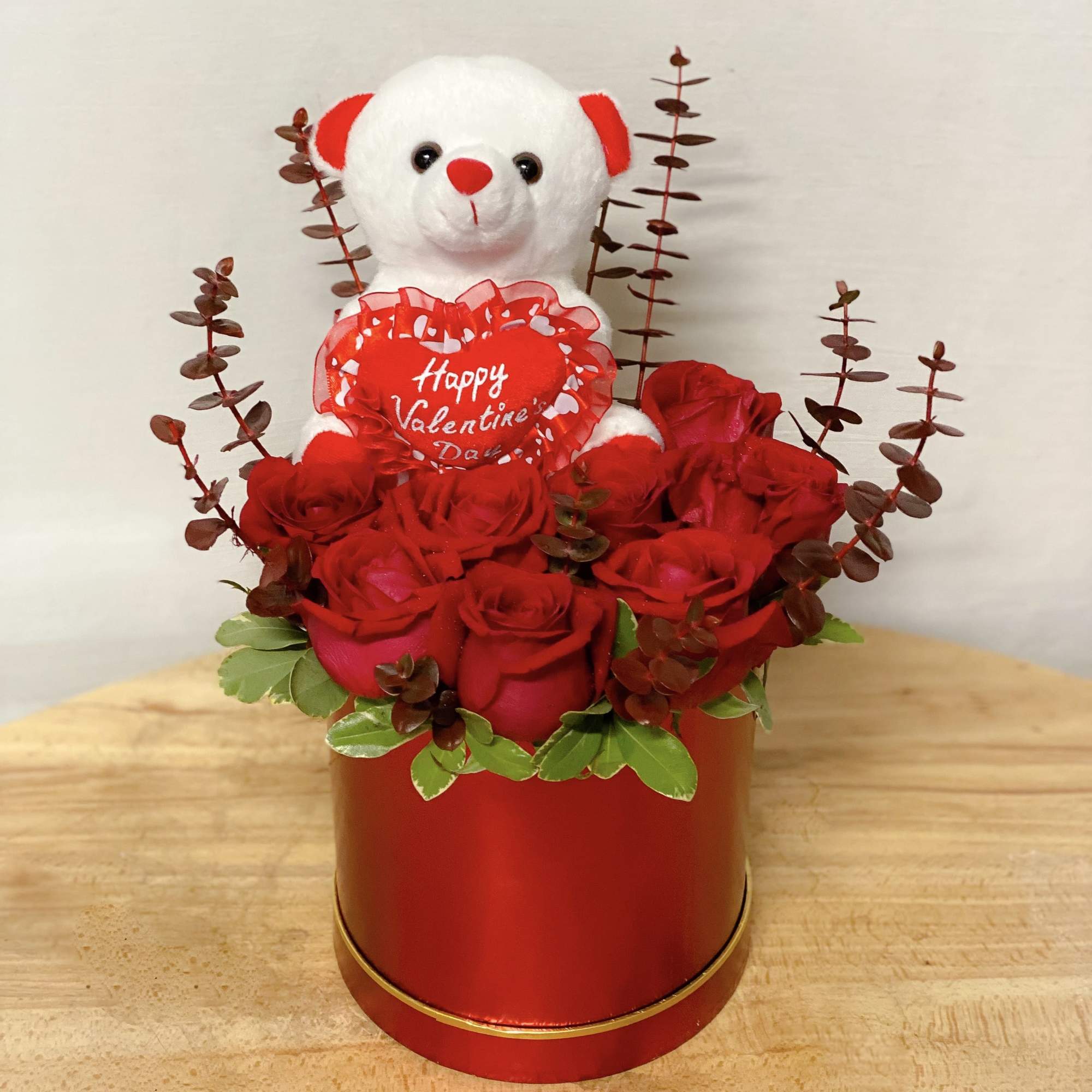 Red roses in a round box with a teddy bear holding a Valentine heart