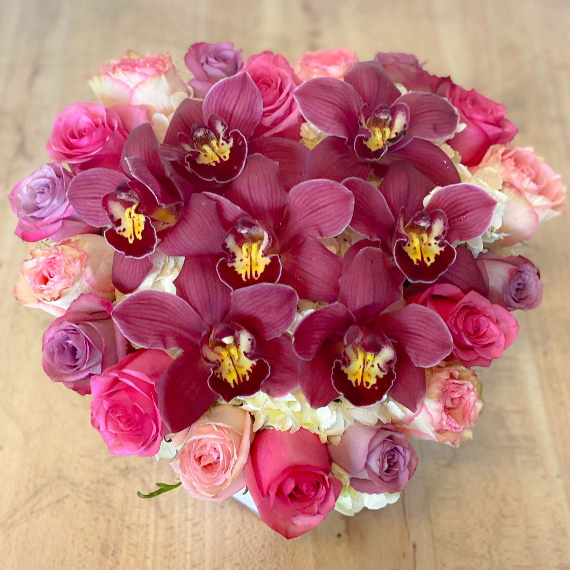 Pink and purple roses with burgundy orchids in a compact bouquet