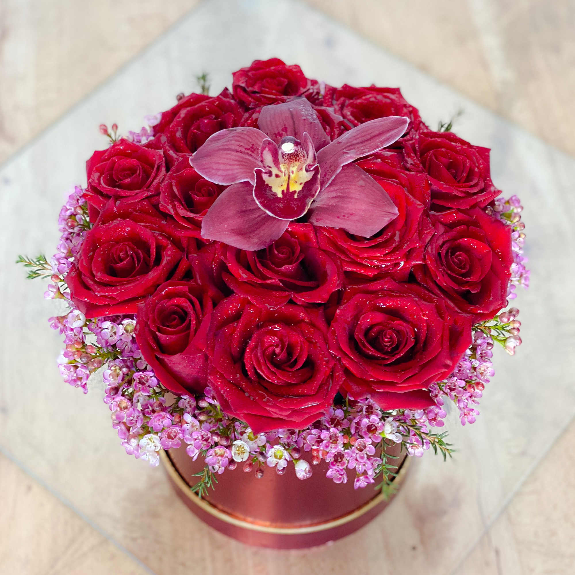 Red roses arranged in a round box with a pink orchid on top