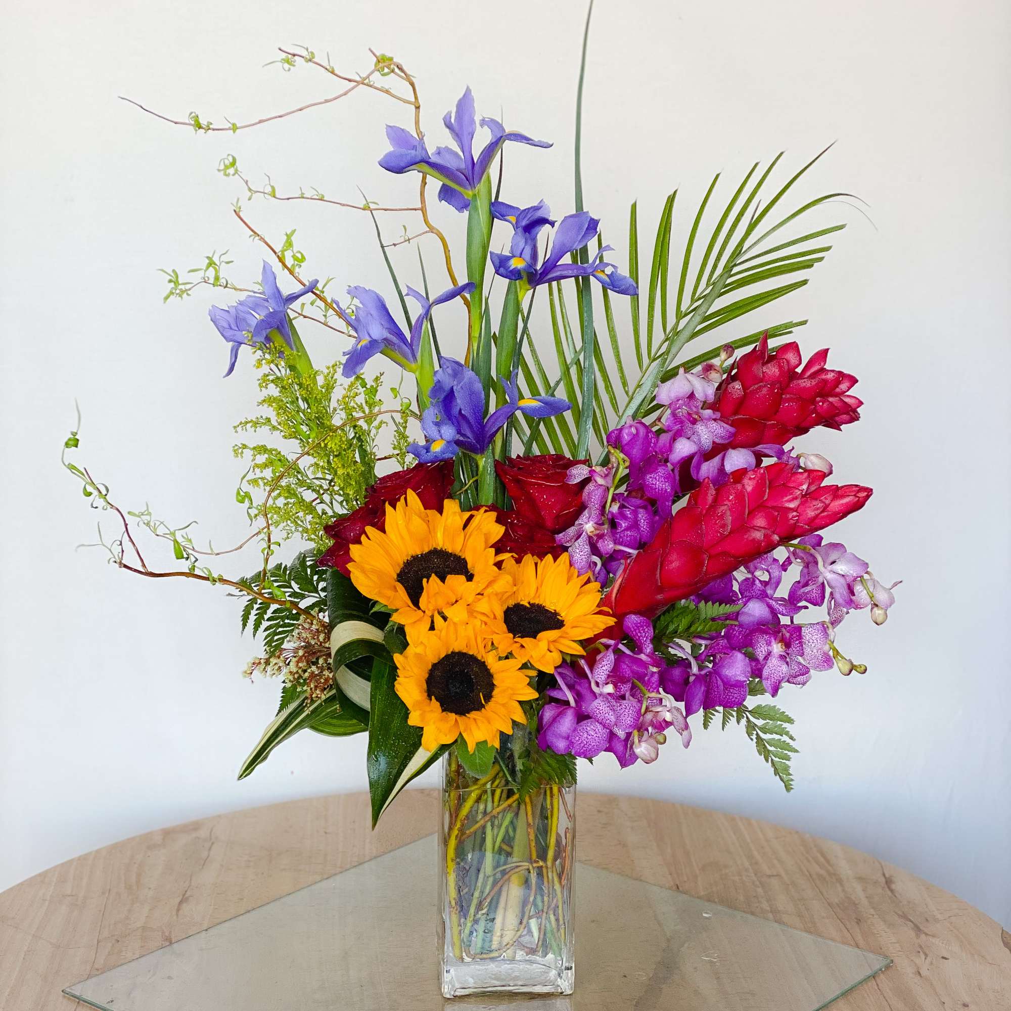 Tall vase arrangement with sunflowers, purple irises, and pink orchids