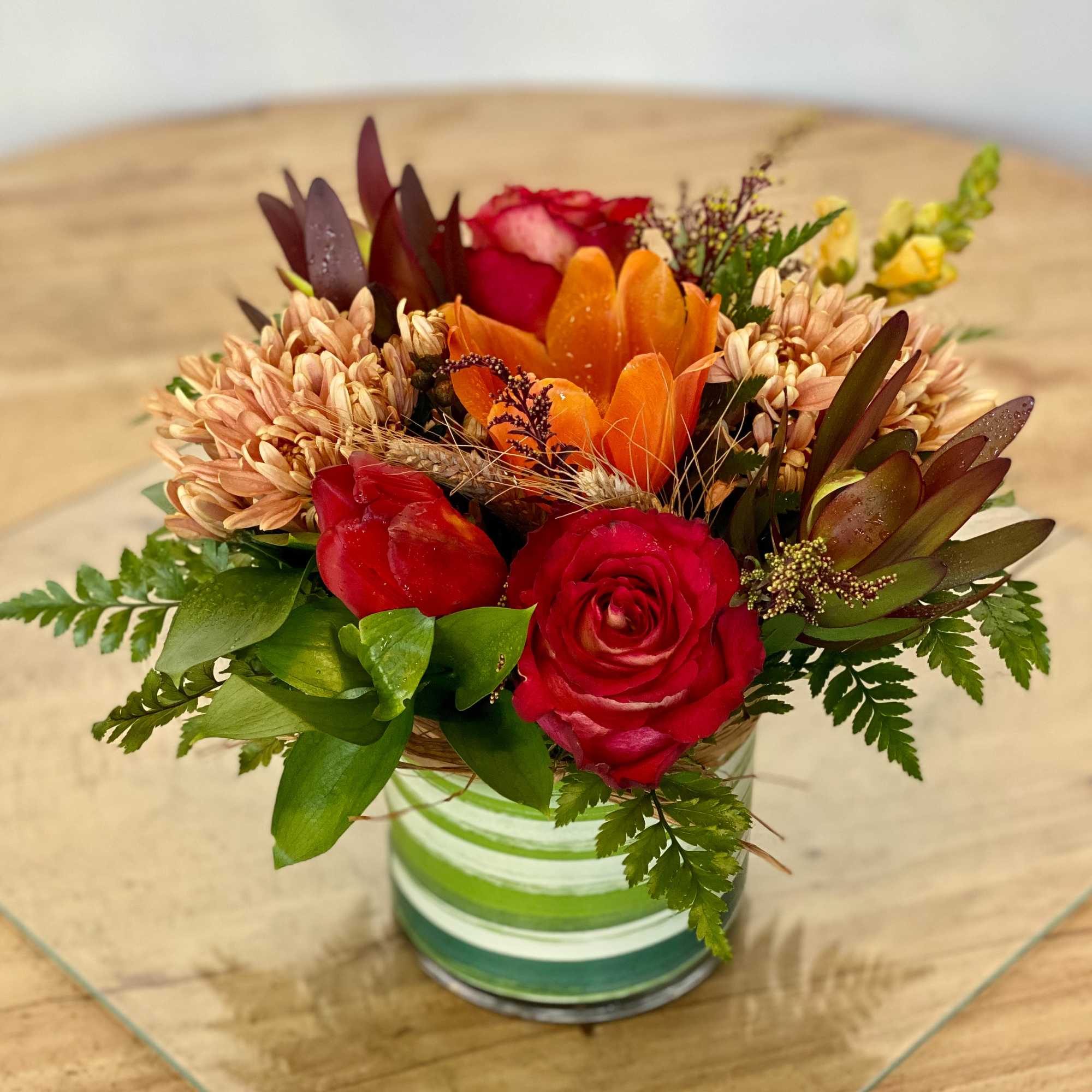 Mixed bouquet of red roses and orange flowers in a striped glass vase