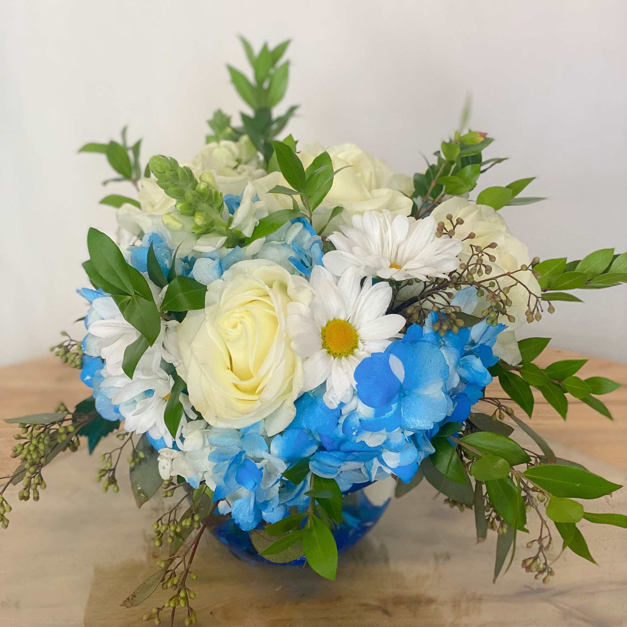 Blue and white flower arrangement with roses and daisies in a vase