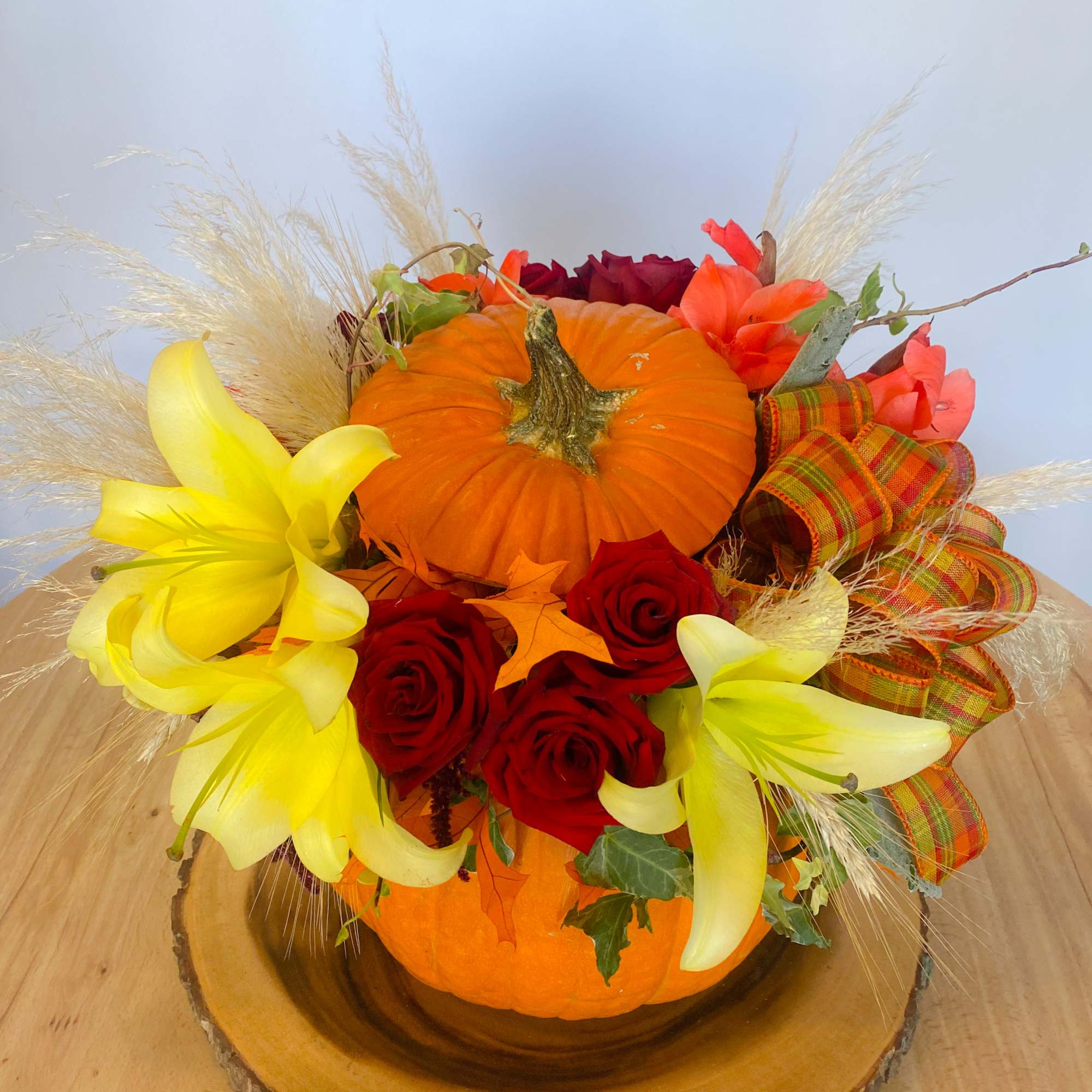 Pumpkin centerpiece with red roses and yellow lilies on a wooden base