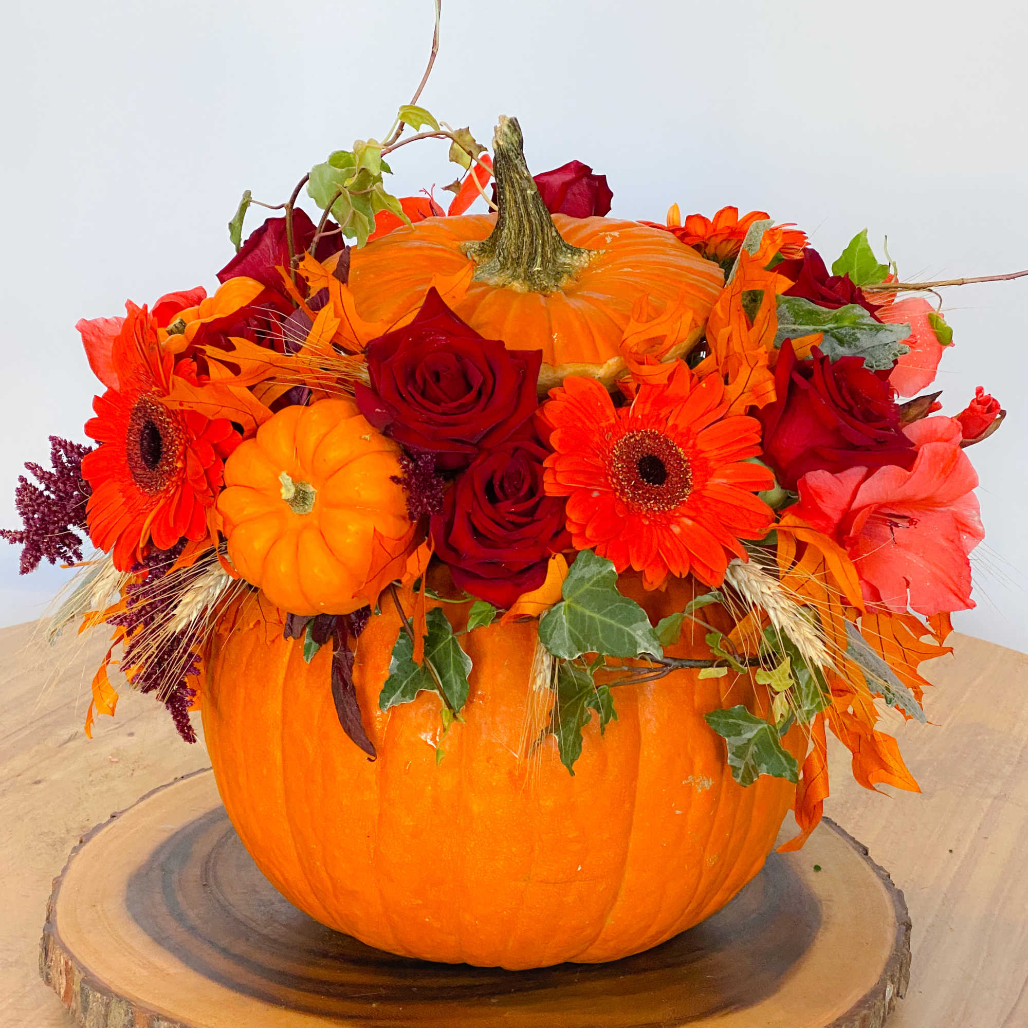 Orange pumpkin centerpiece with red roses and orange daisies
