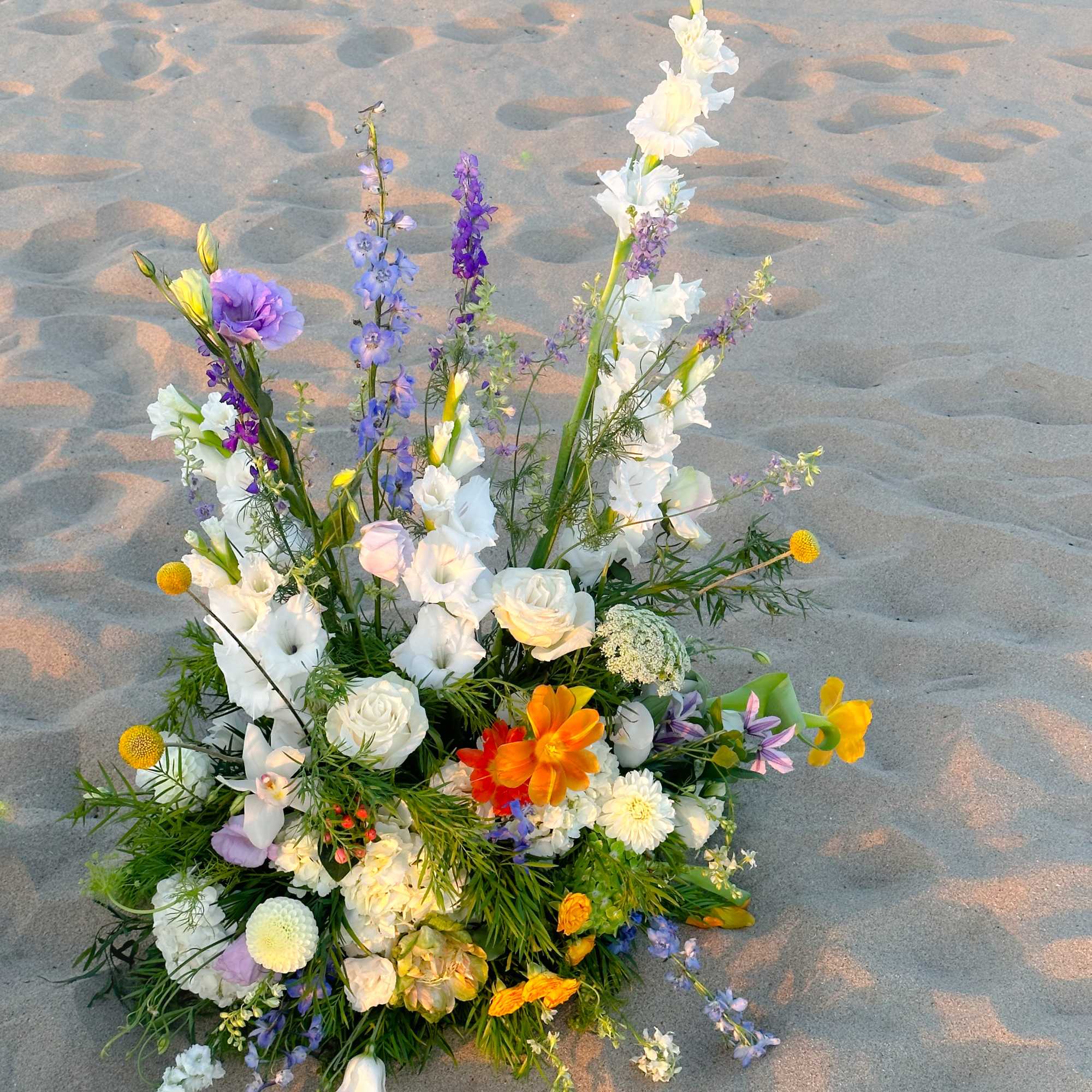 Colorful mixed flower arrangement with tall white and purple blooms on sand