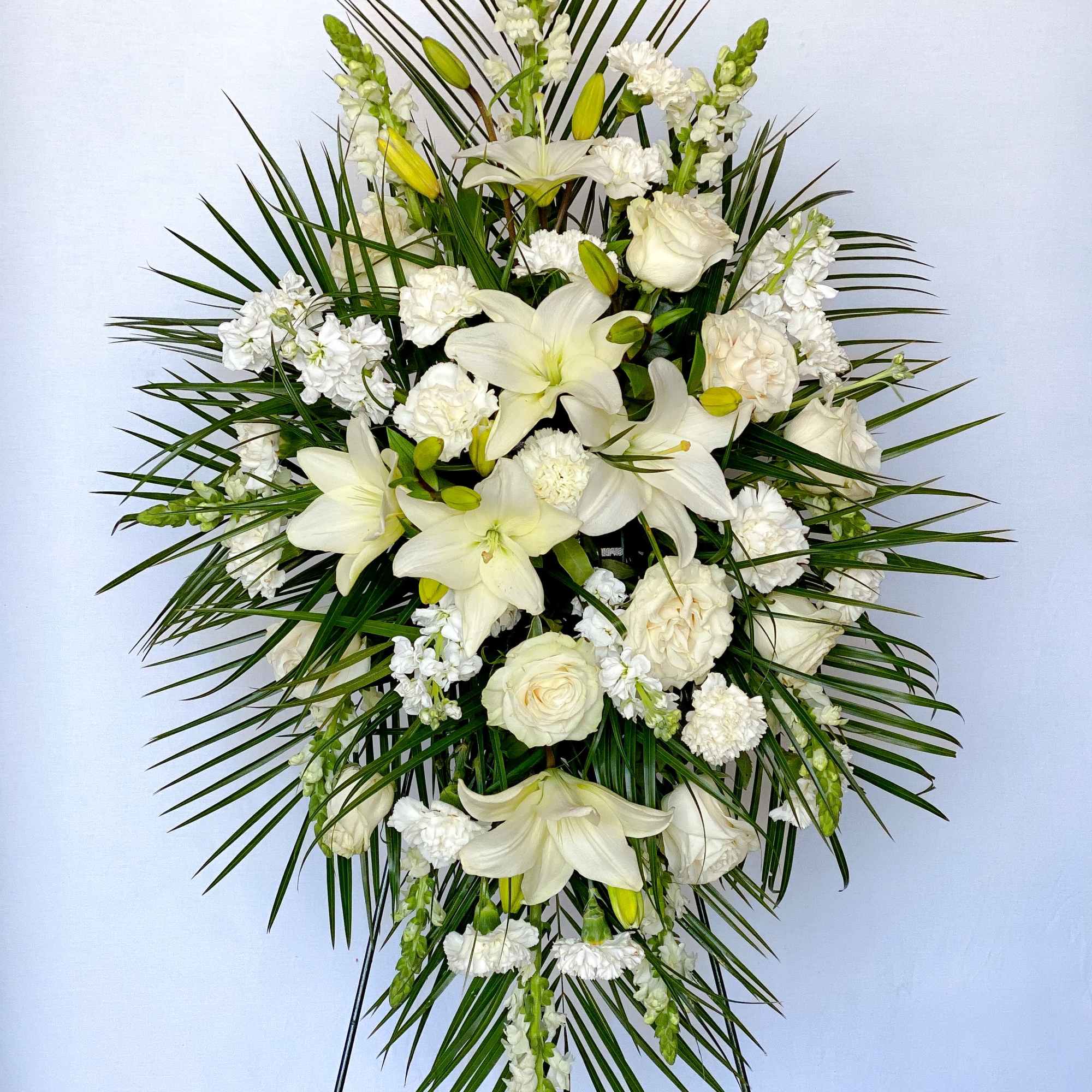 White floral standing spray with lilies and roses on a palm backdrop
