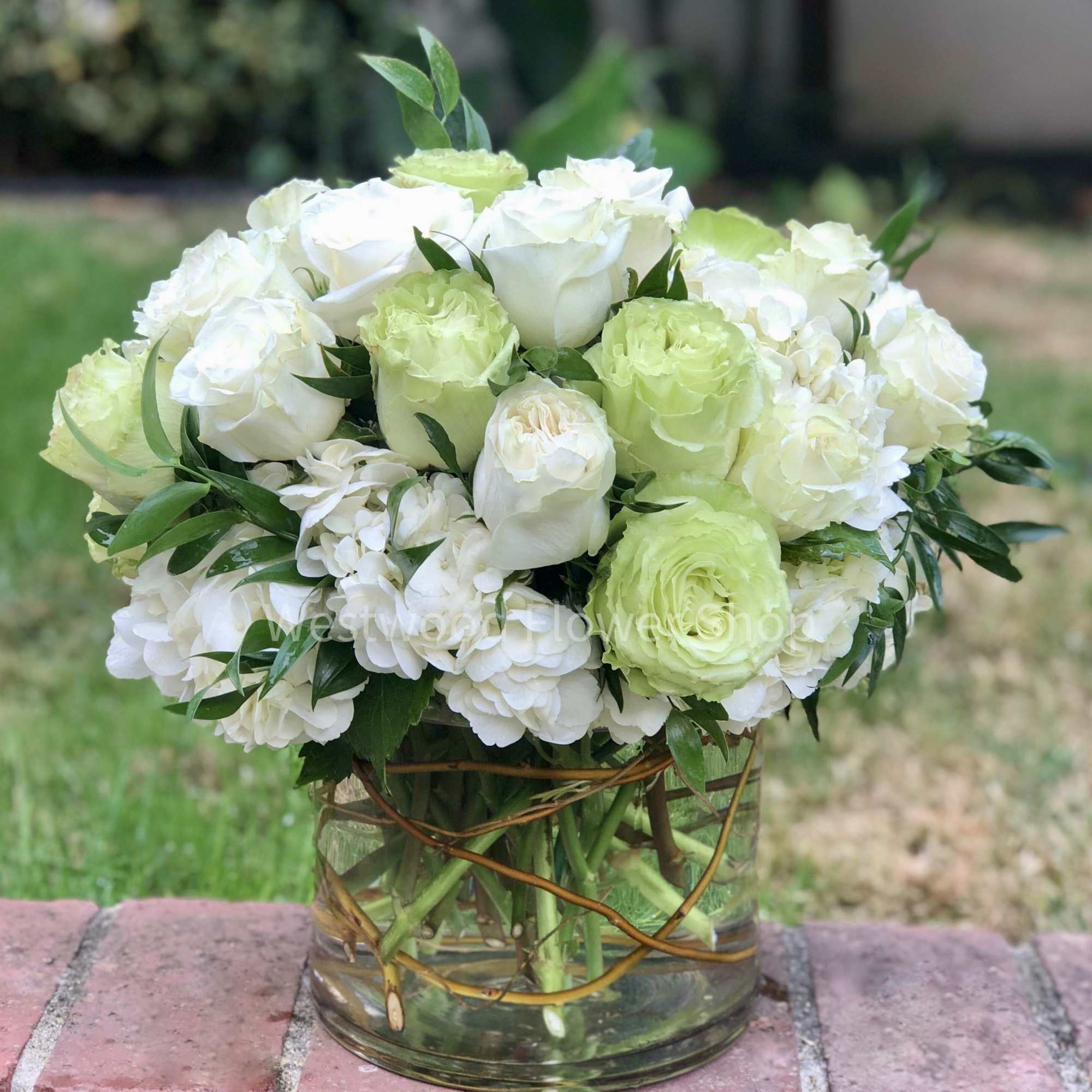 White and pale green roses arranged in a clear glass vase