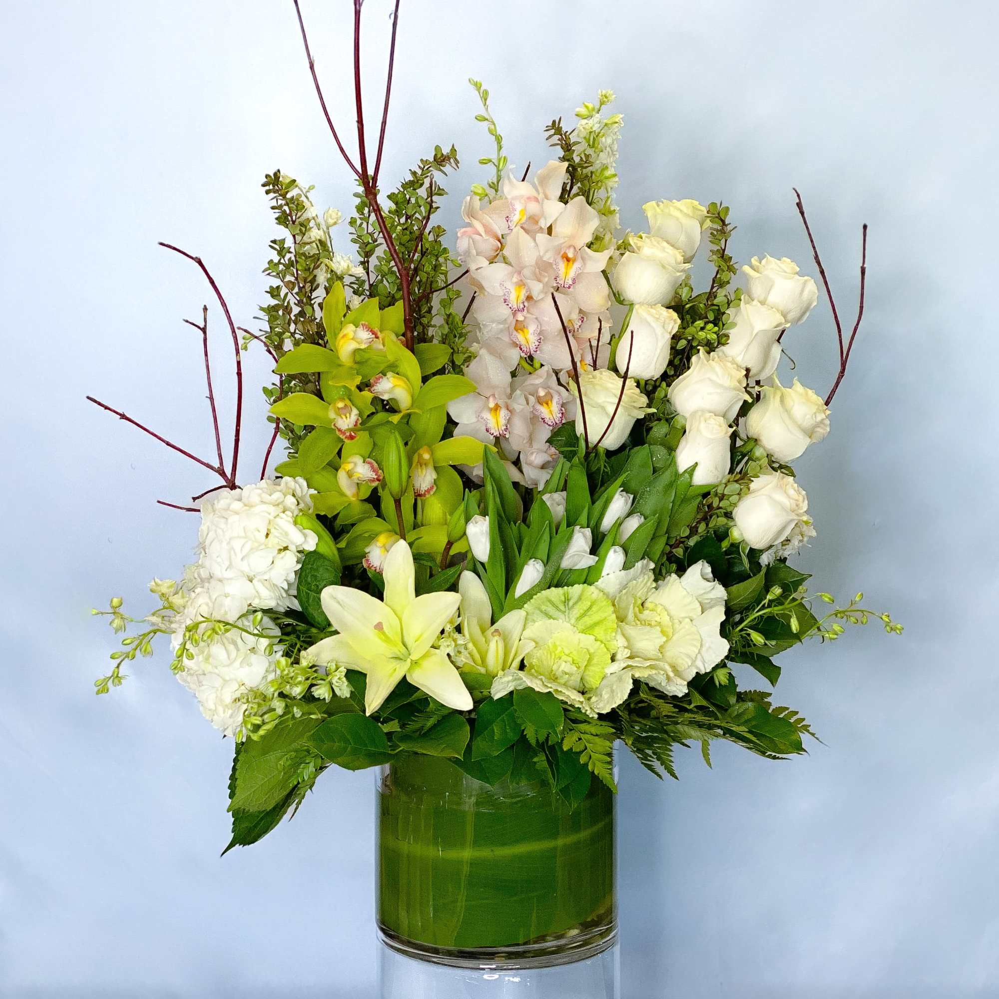 White roses, orchids, and lilies arranged in a green glass vase