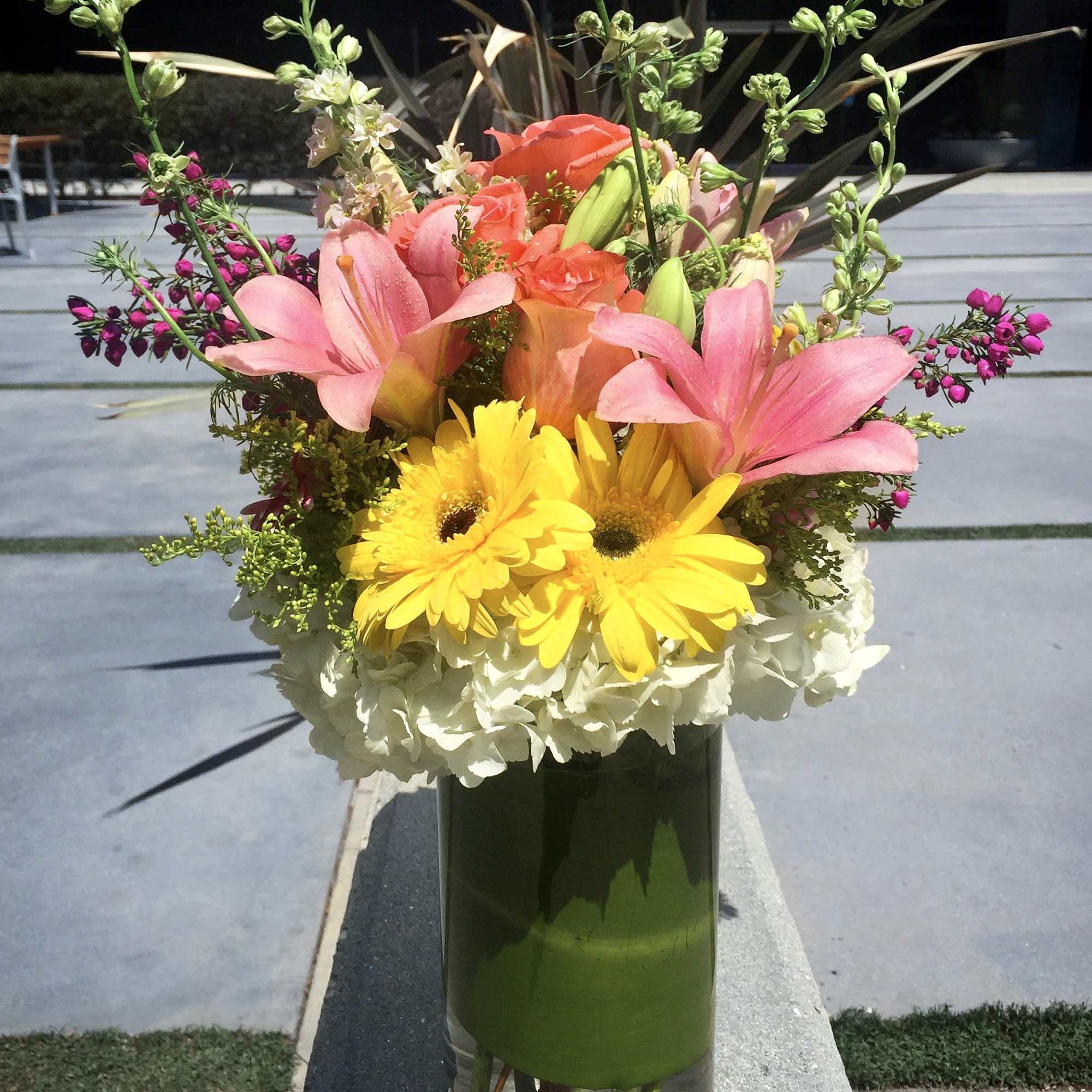 Colorful bouquet with pink lilies, yellow daisies, and roses in a glass vase