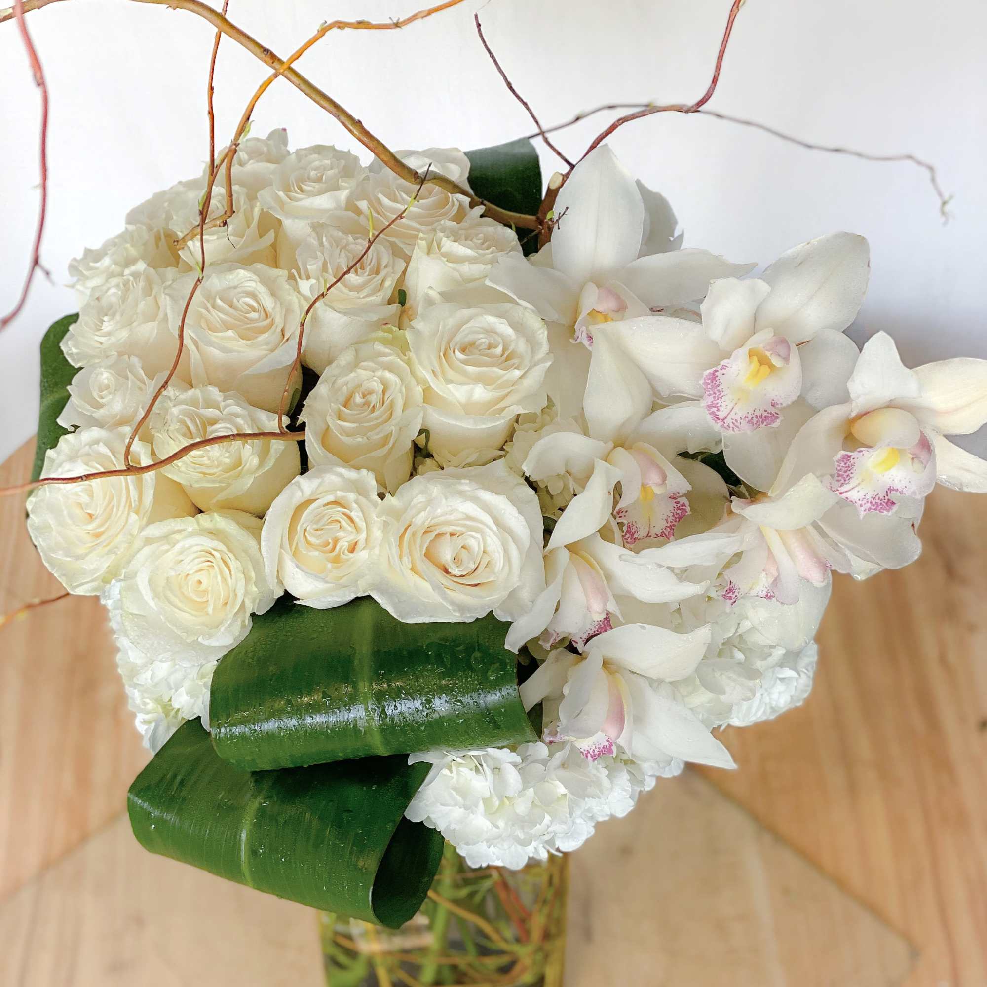 White roses and orchids arranged in a glass vase with curly branches