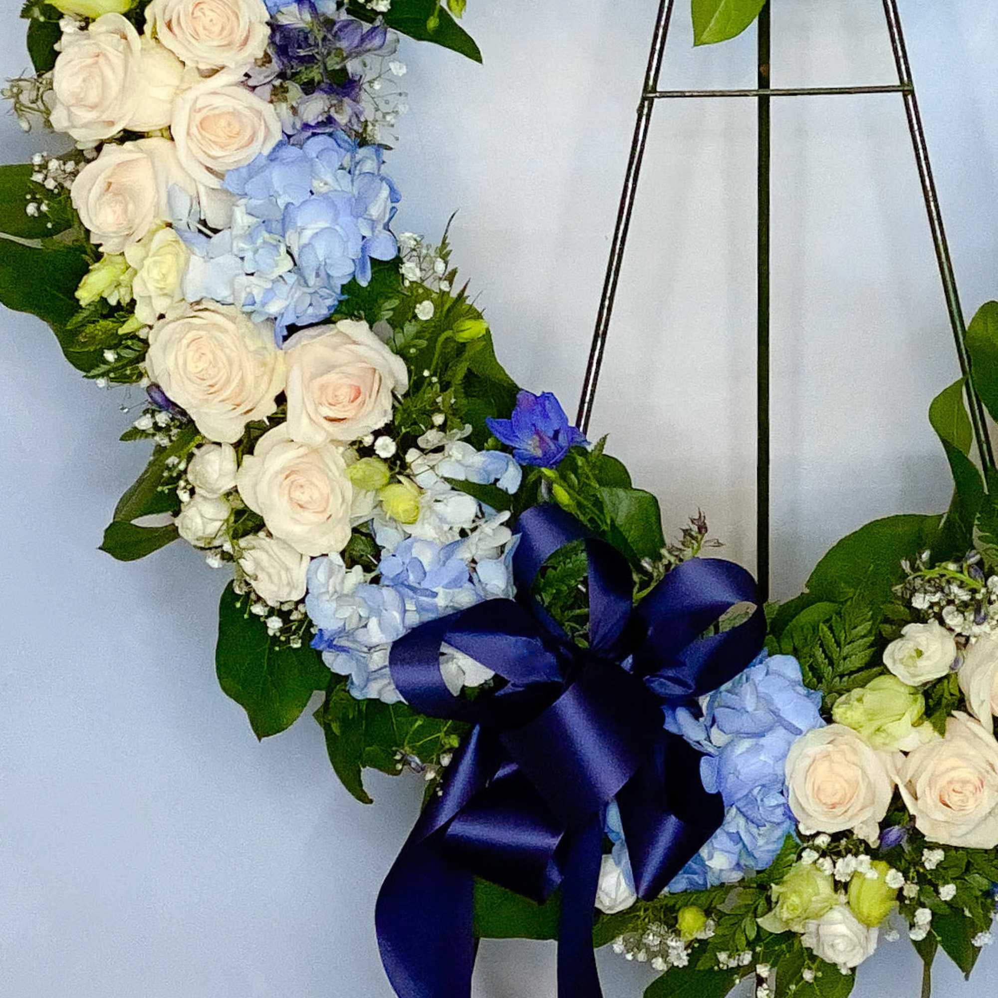 Floral wreath with white roses, blue hydrangeas, and a navy ribbon